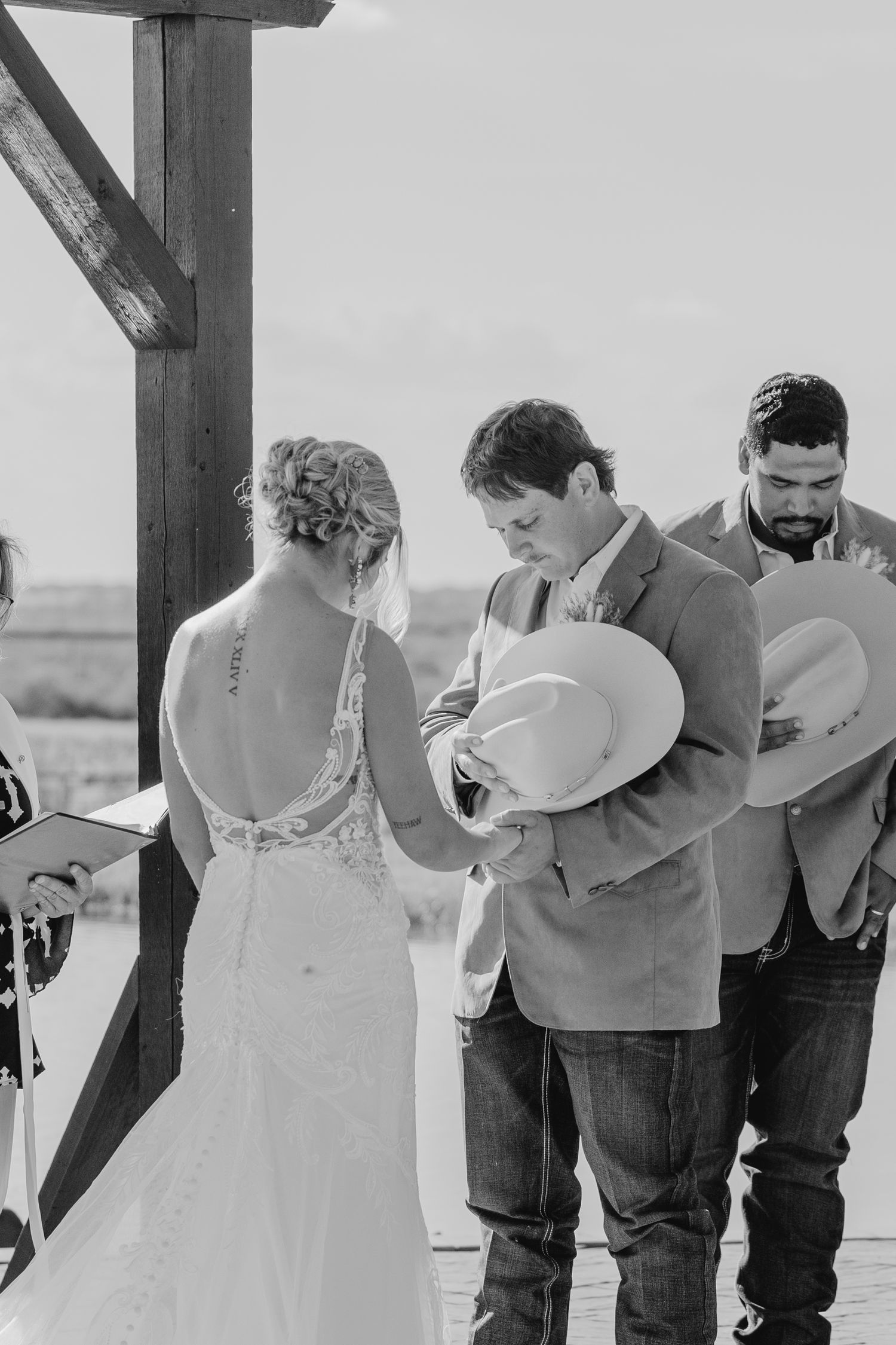 Black and white wedding ceremony with couple exchanging vows under wooden structure.
