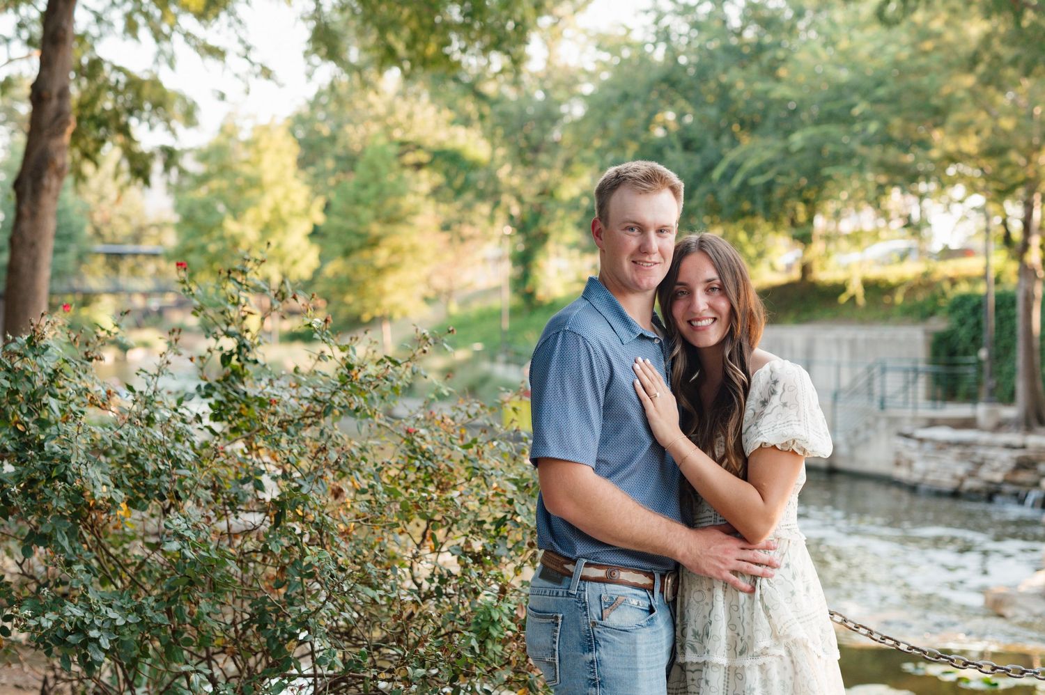 A couple embraces outdoors during a romantic photo session in a natural setting with trees and sunlight.
