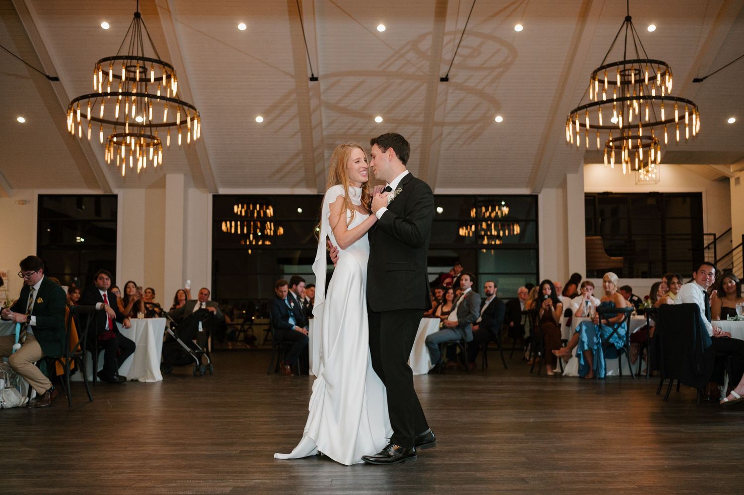 A couple shares their first dance under elegant chandeliers at their wedding reception.