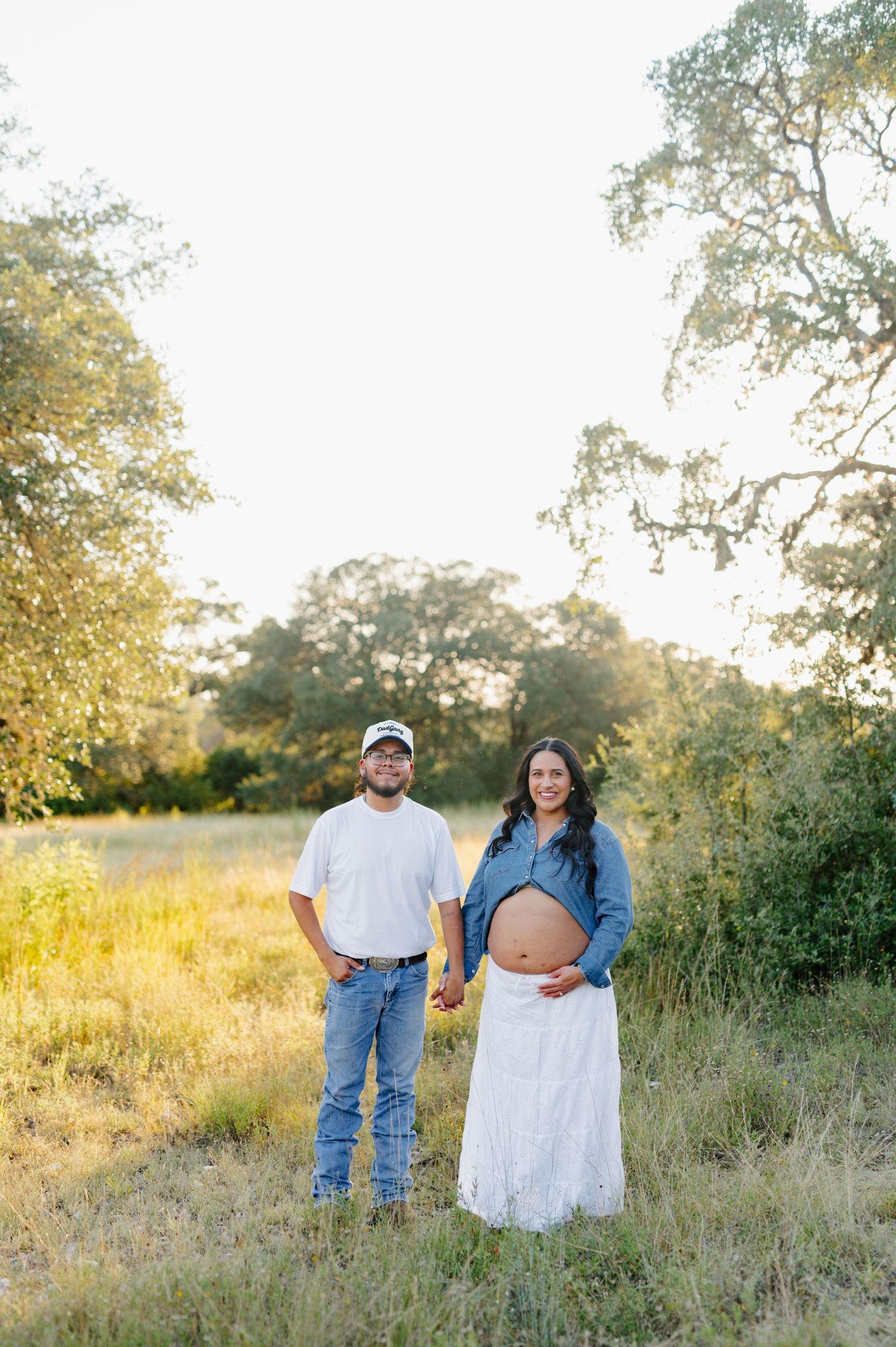 A couple's portrait session in a golden field with trees and natural lighting at sunset.