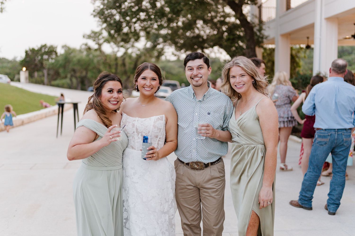 Wedding party in sage green dresses and navy suits posing outdoors.