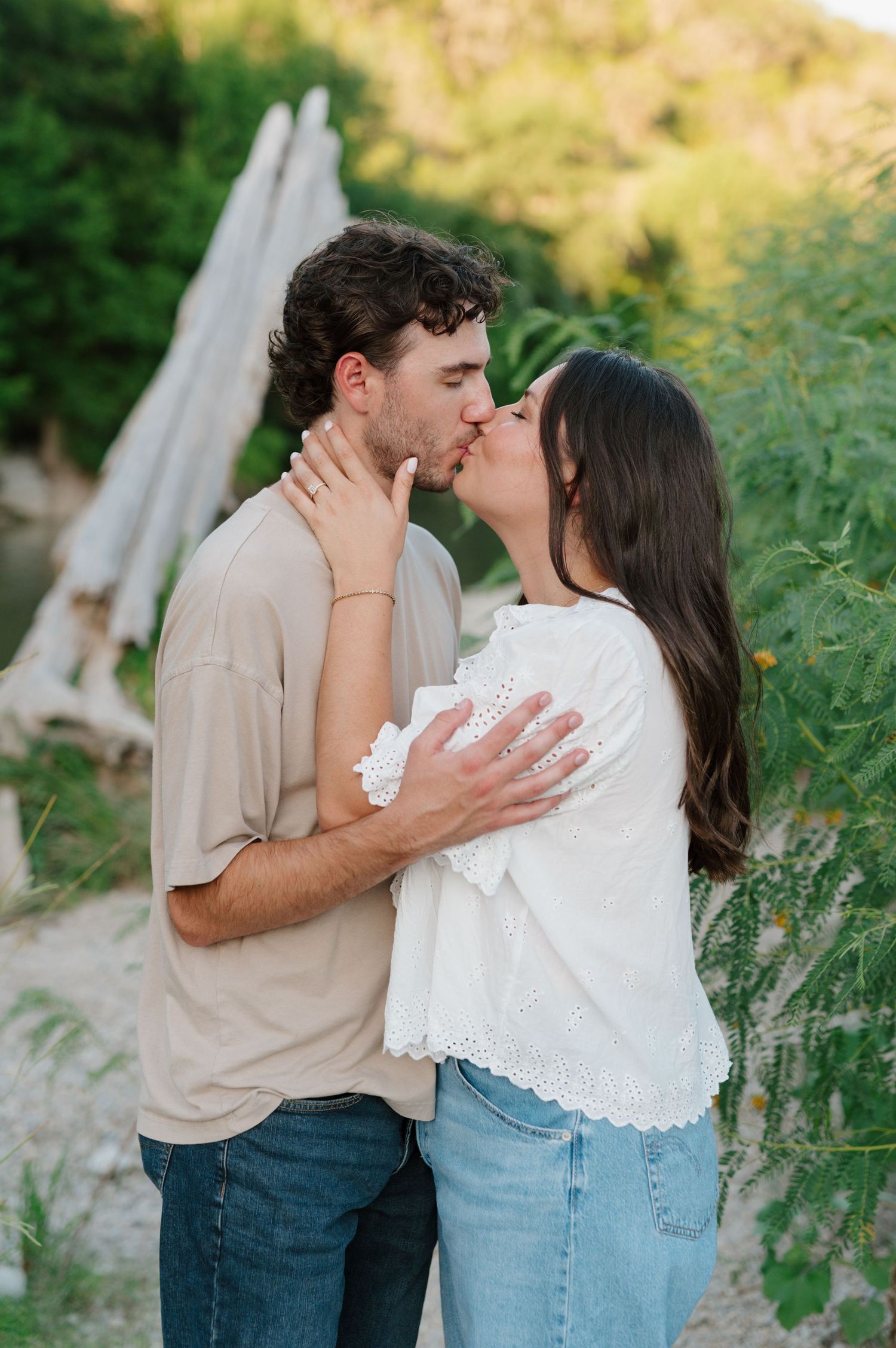 A couple shares intimate kisses during their outdoor photoshoot in a natural setting.