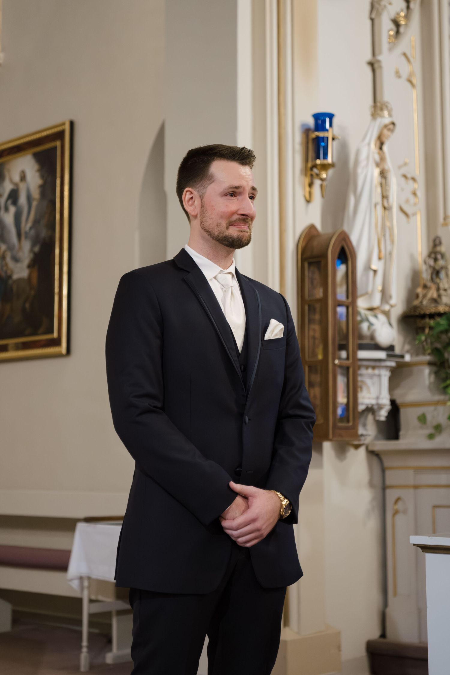 A formal wedding ceremony takes place in an ornate church interior with decorative wall details and blue accents.