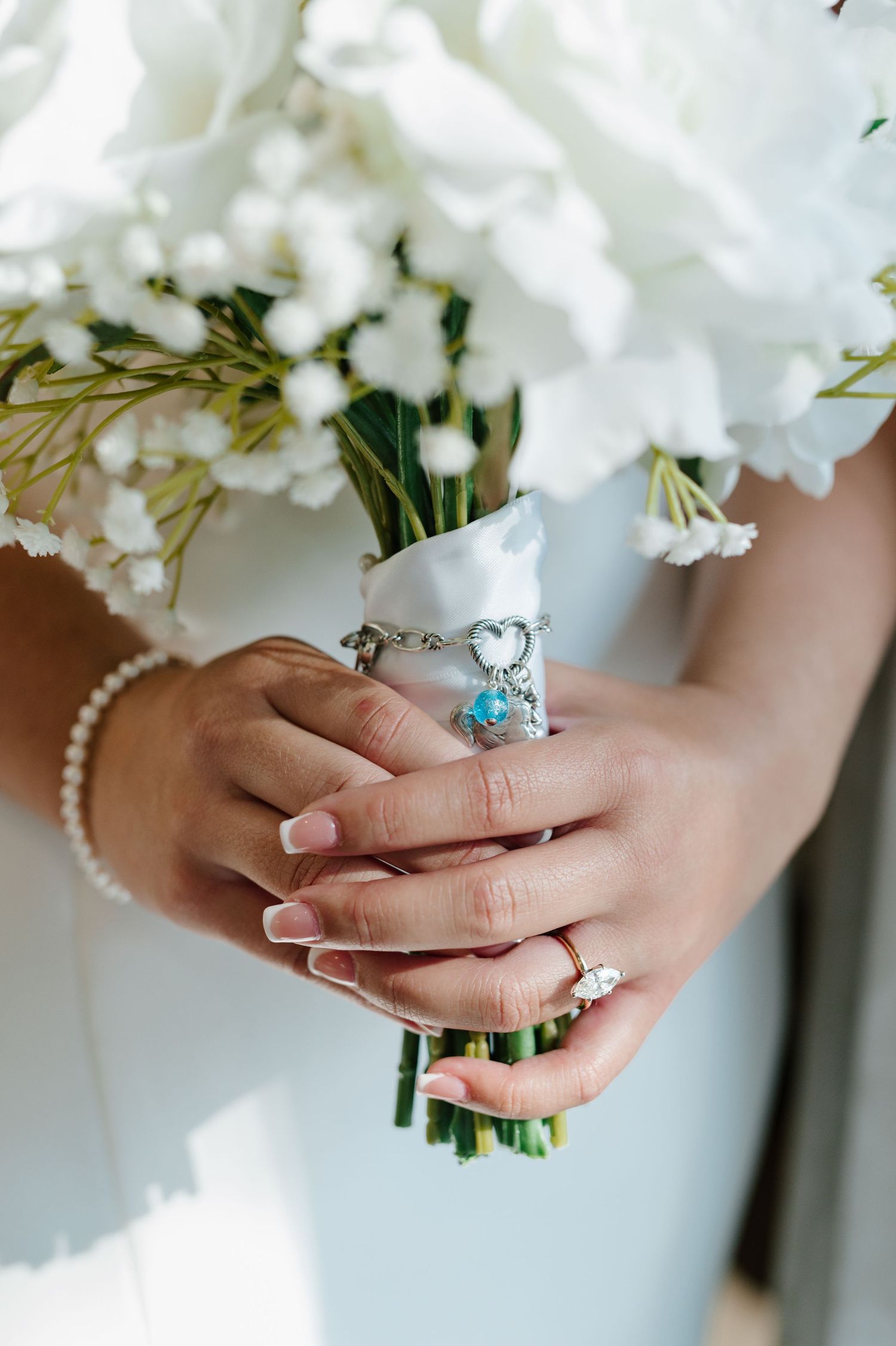 Close up of hands wearing a pearl bracelet and holding delicate white flowers with an engagement ring.