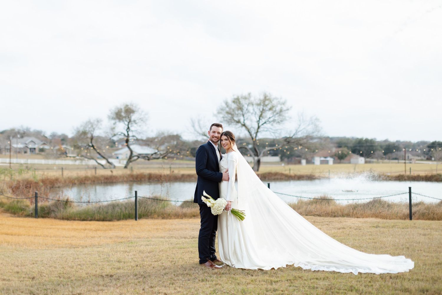 A couple in wedding attire stands on a wooden boardwalk overlooking a scenic marsh landscape during golden hour.