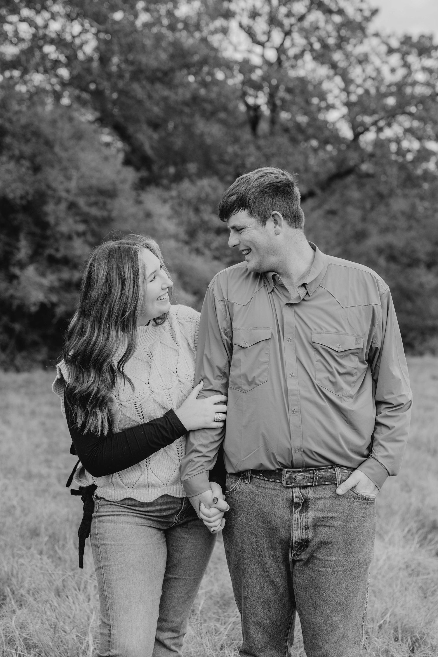 A black and white portrait of a couple sharing a laugh in a field.