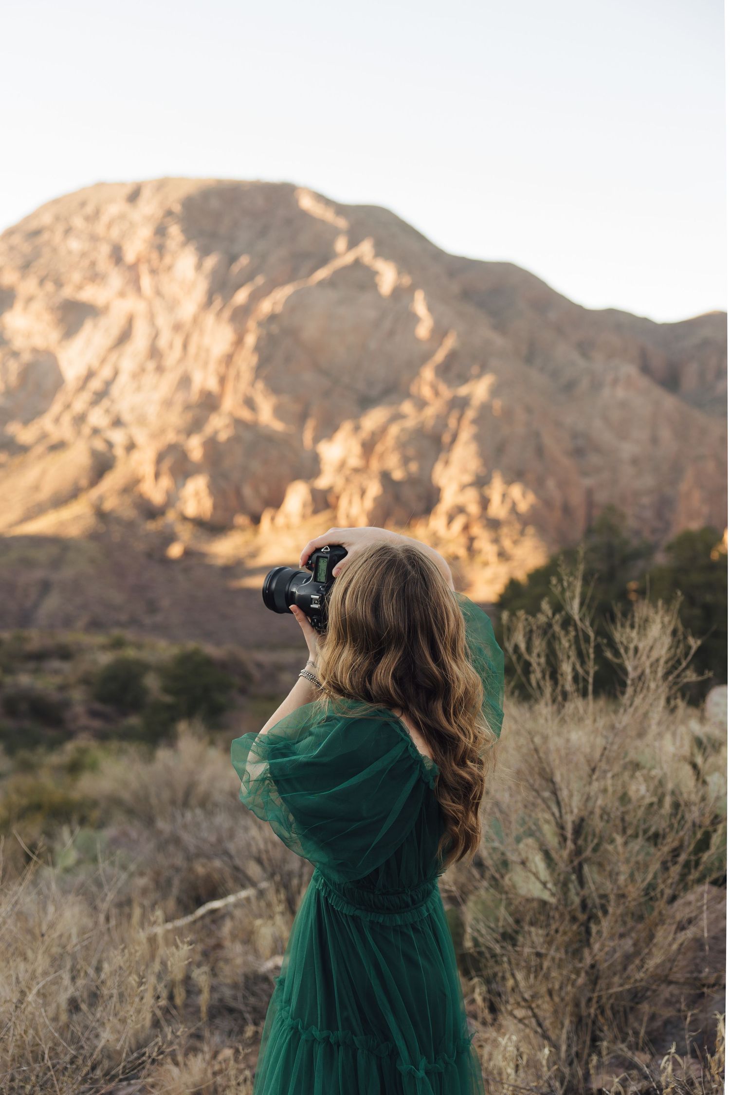 Person wearing green dress photographs rocky desert landscape at sunset.