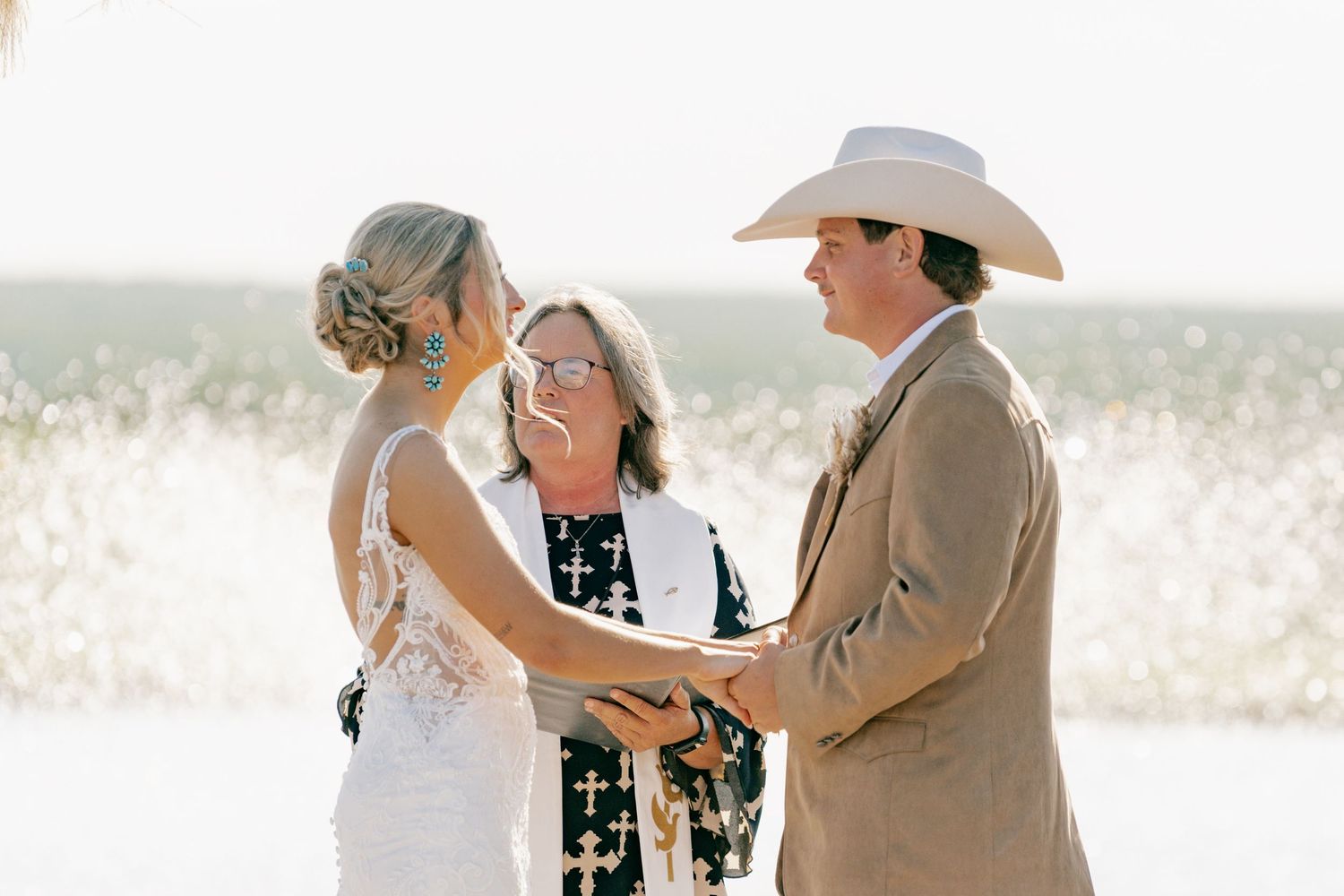 Outdoor wedding ceremony with couple and officiant against scenic landscape.