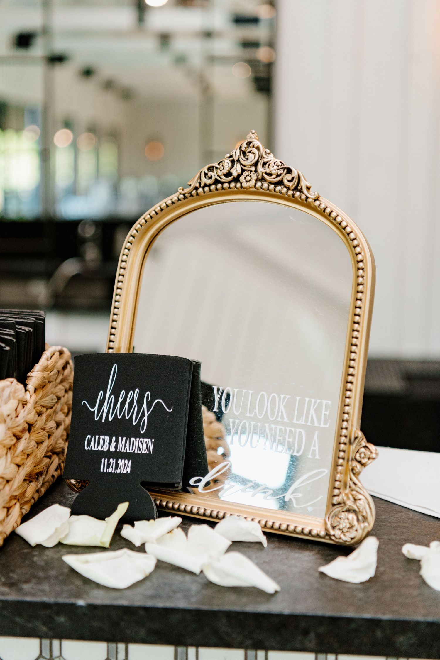Elegant gold ornate mirror frame with black chalkboard signs and scattered white rose petals on dark surface.