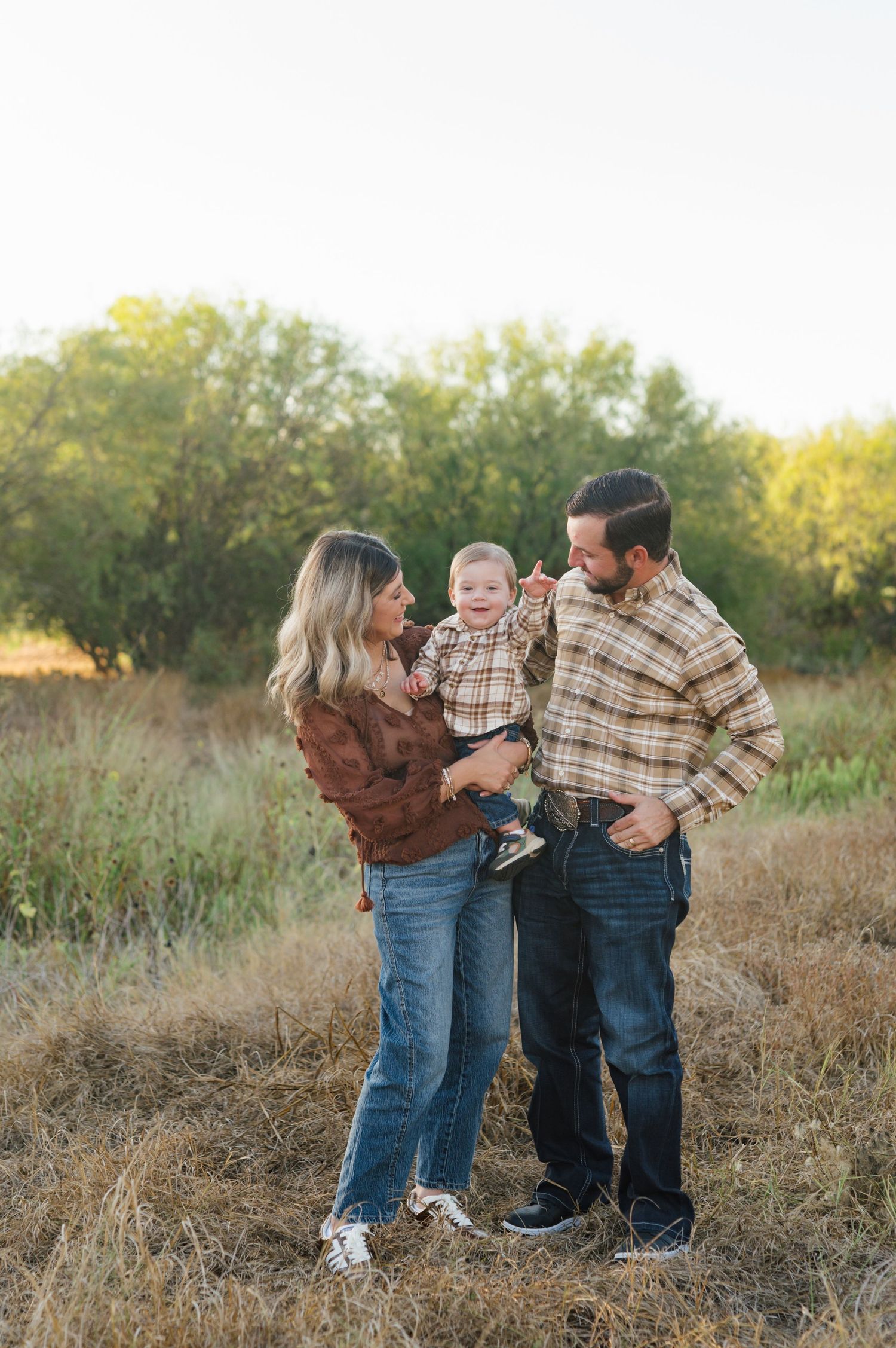A family stands together in a field during golden hour wearing coordinating plaid and brown outfits.