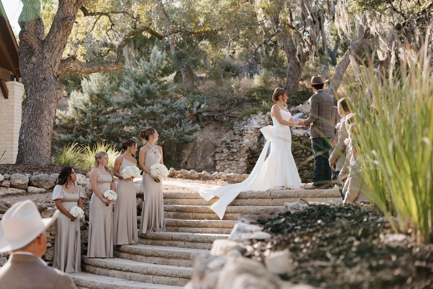 Wedding party arranged on stone steps in an outdoor garden setting.