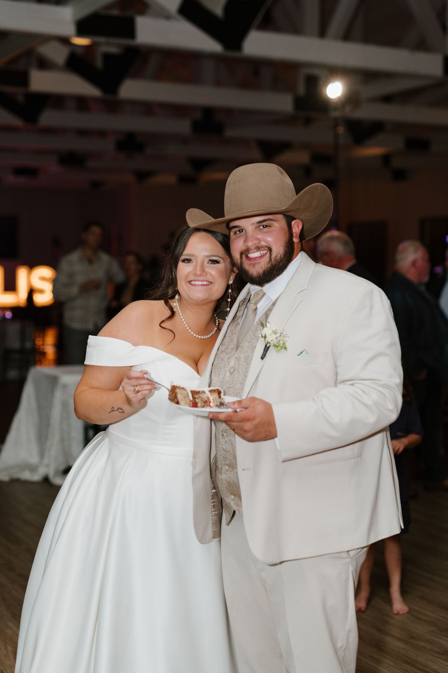A couple in ivory wedding attire holding a dessert plate together at their reception celebration.