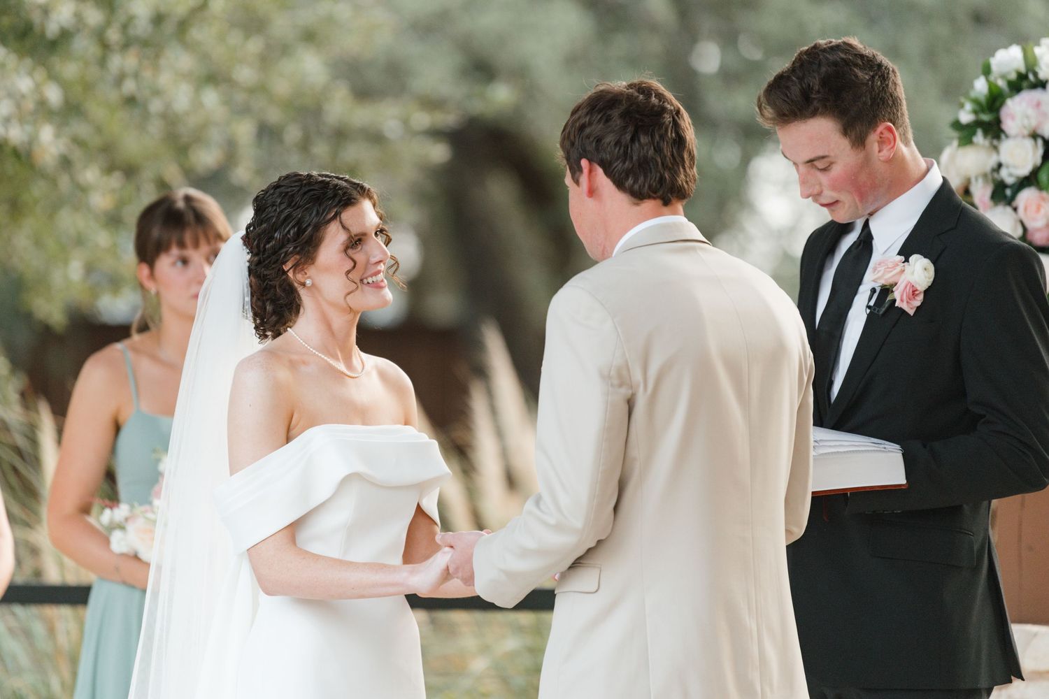 Wedding ceremony taking place outdoors with couple exchanging vows under trees.