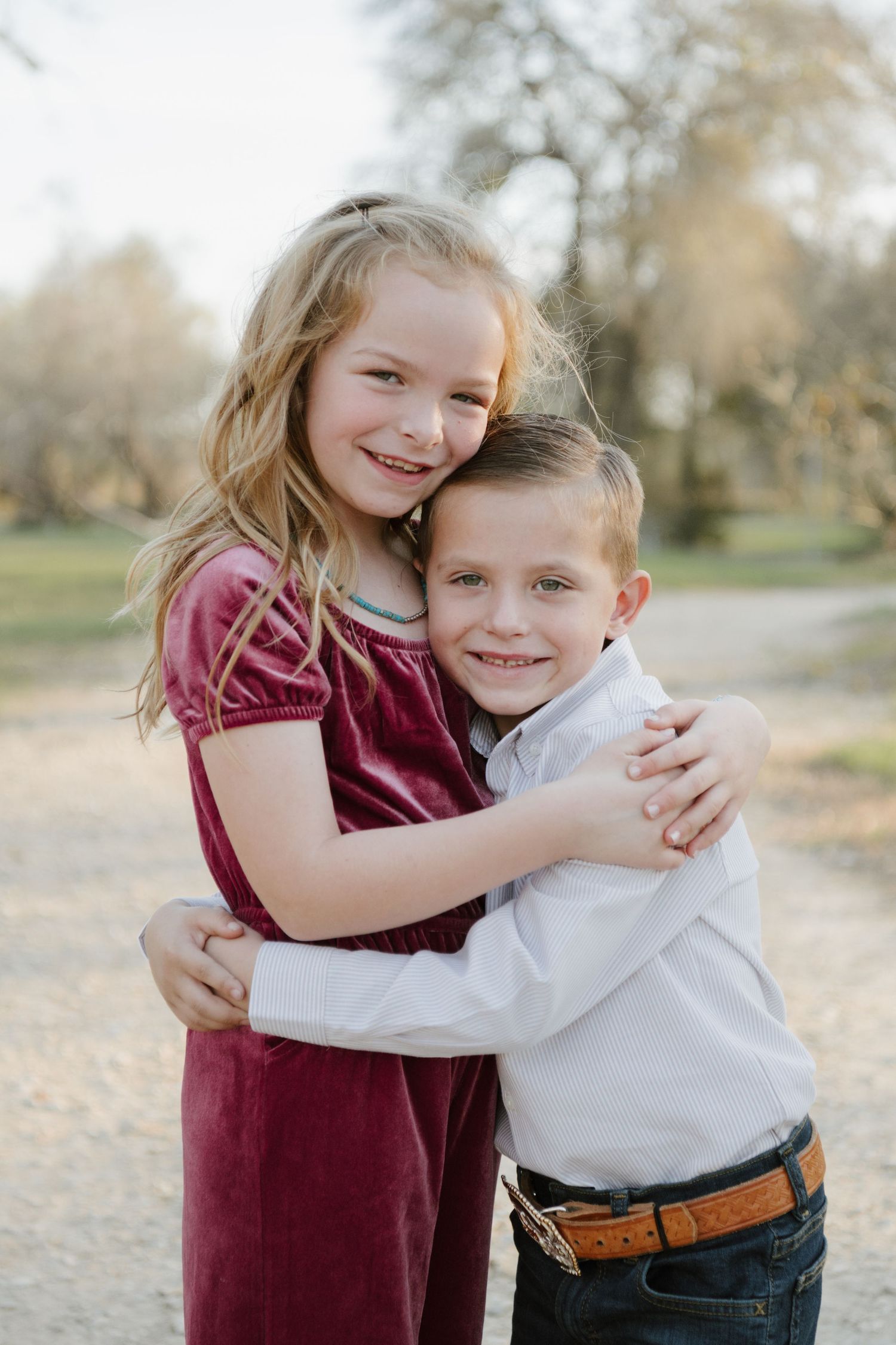 Two young siblings share a sweet embrace outdoors in burgundy and white outfits during an autumn photoshoot.