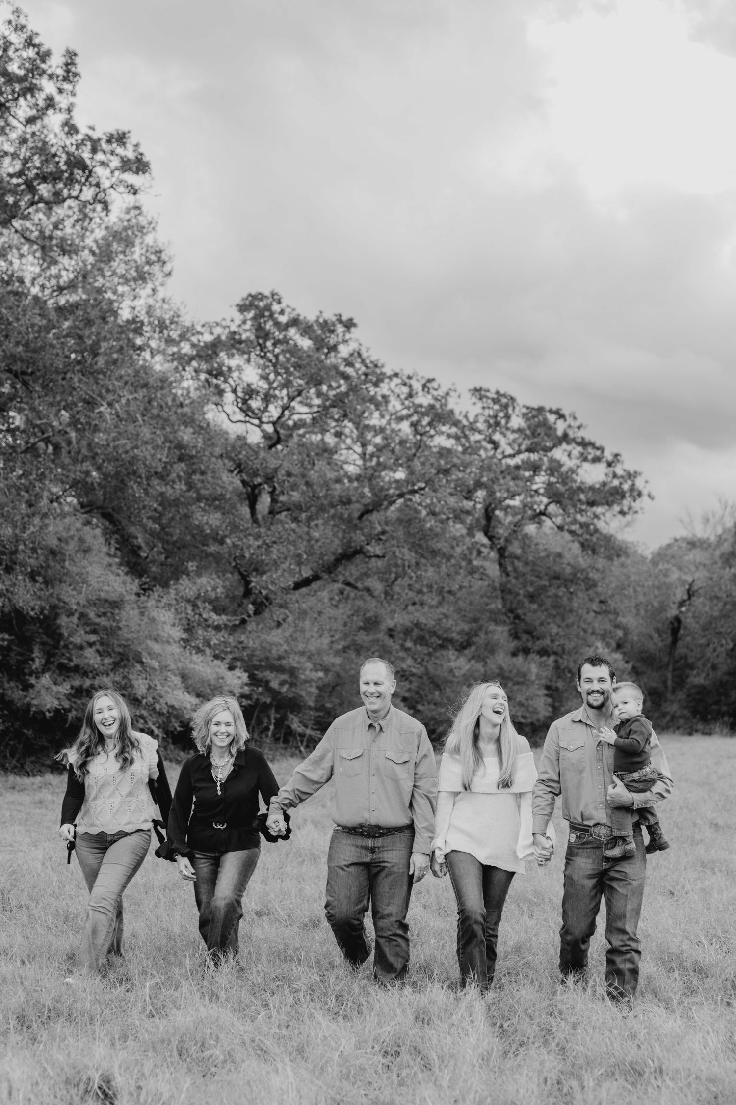 A group walks together through a field during an outdoor black and white photo session.