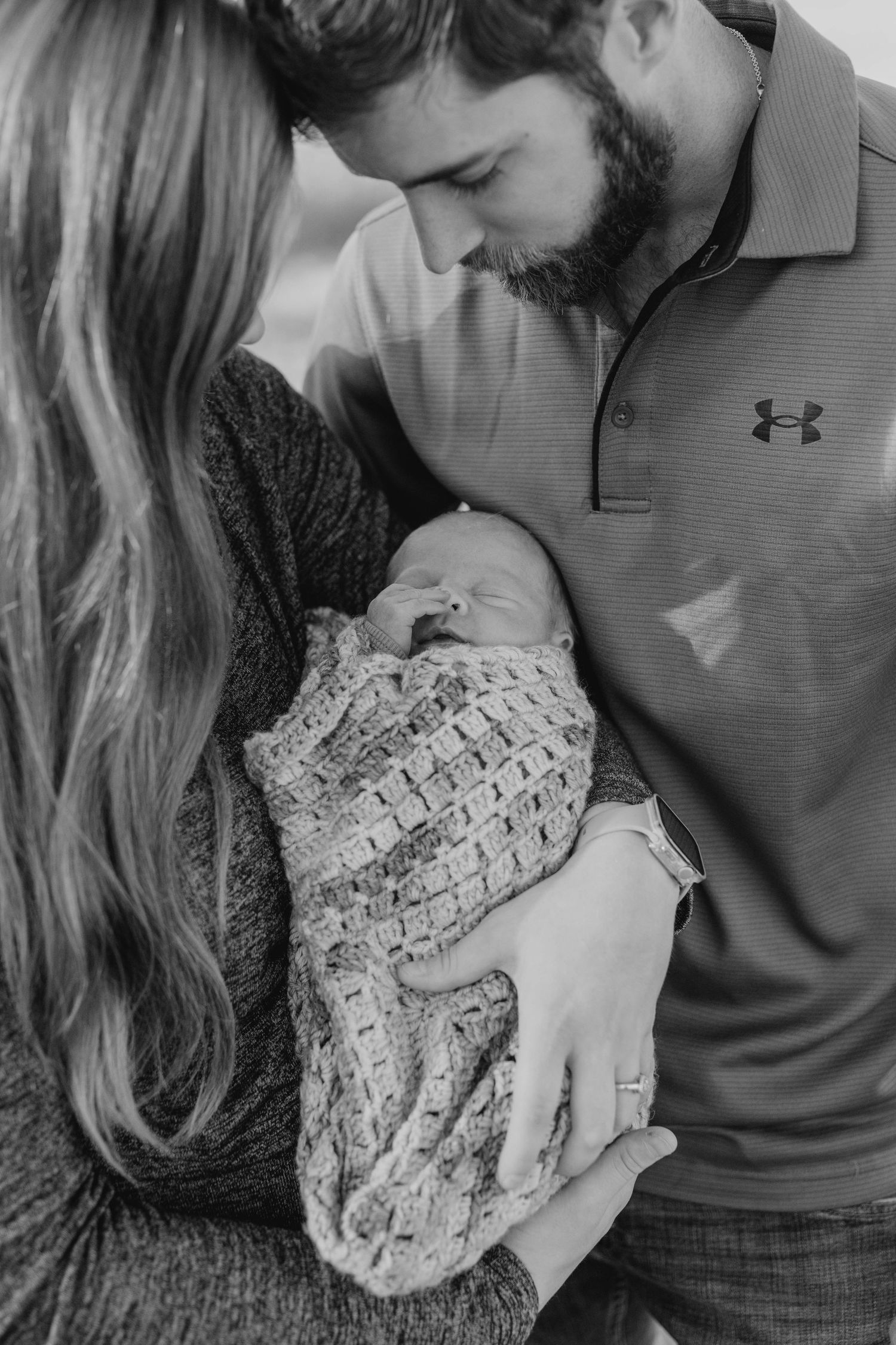 Black and white portrait of parents gazing at their swaddled newborn baby.