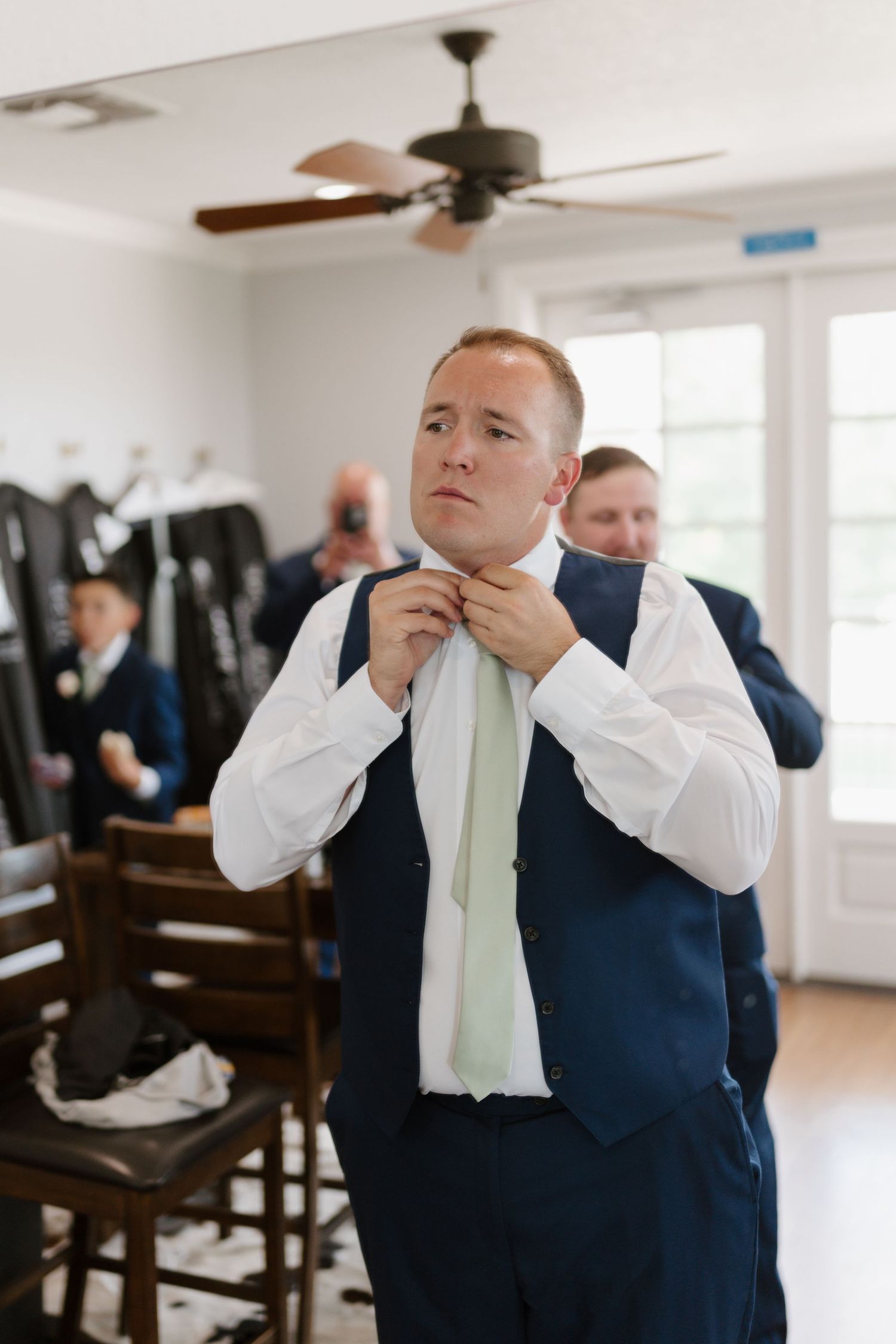 Emotional moment as a man in navy suit adjusts his tie while getting ready in a bright indoor venue.
