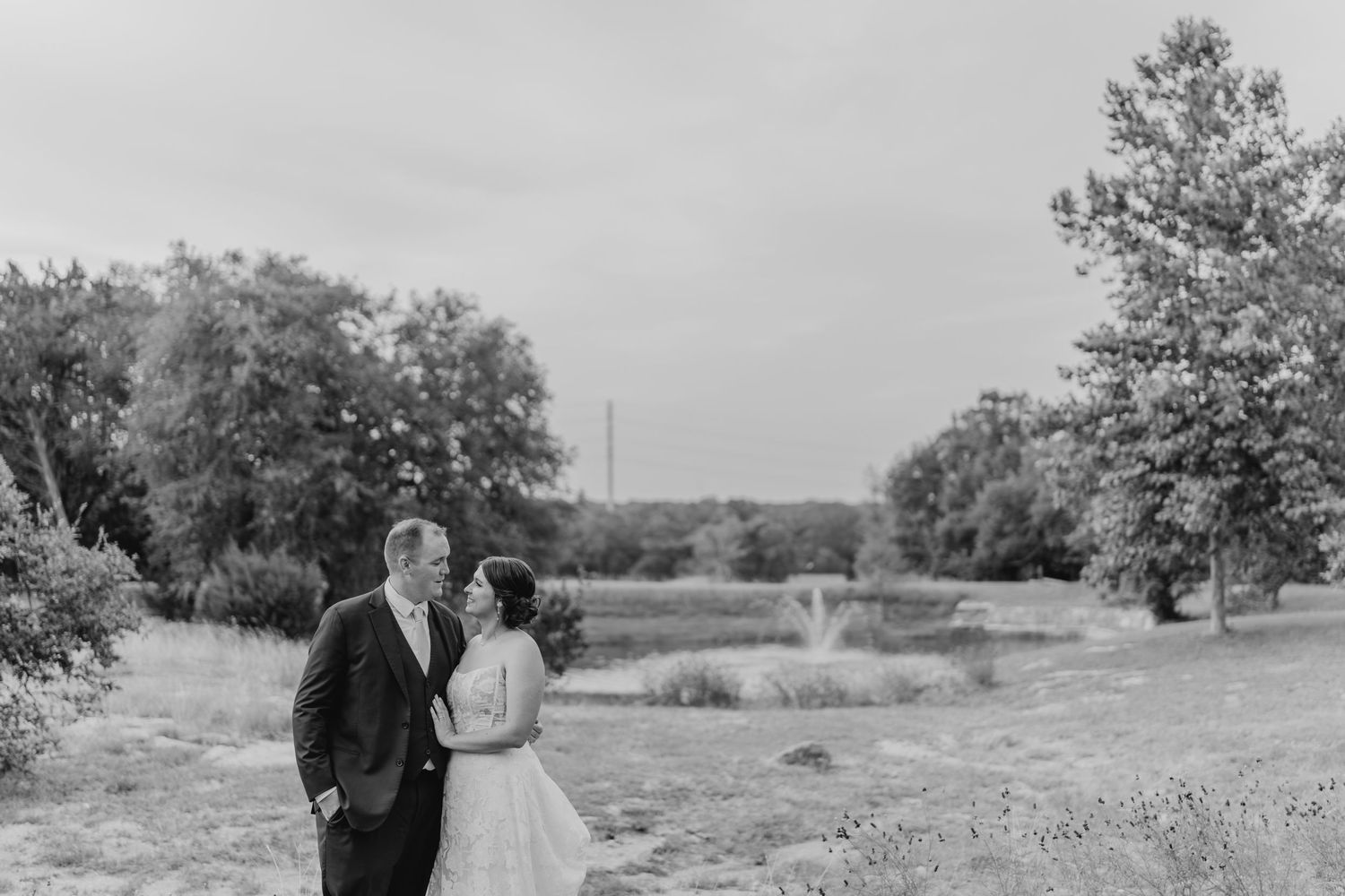 Wedding couple walks together through a scenic outdoor setting with trees.