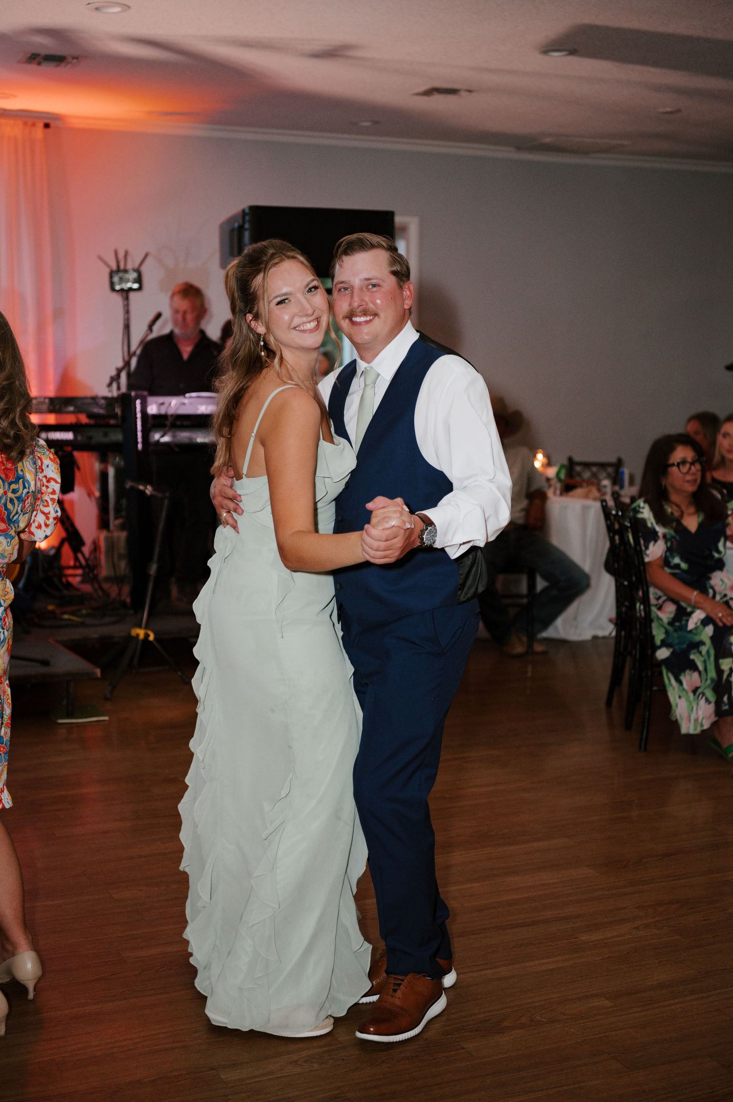 Wedding guests dance on a wooden floor at an evening reception with warm lighting.