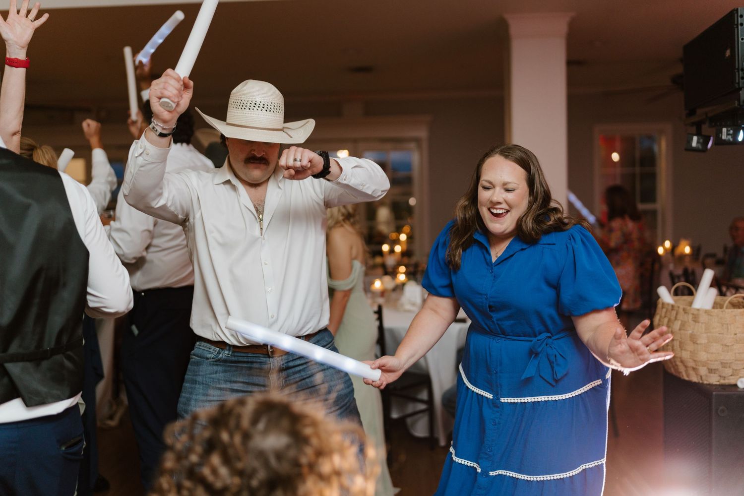 Wedding guests dancing and celebrating with their hands in the air at a lively reception.