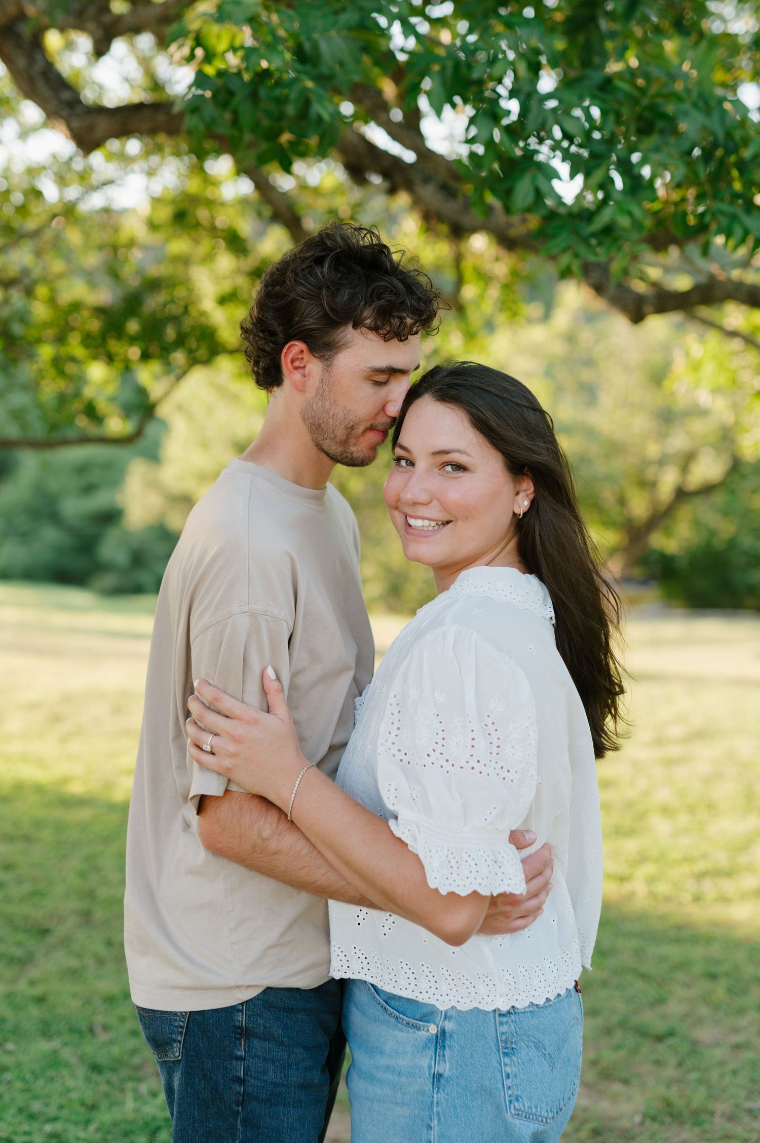 A couple in casual attire sharing tender moments in a sunny park setting.