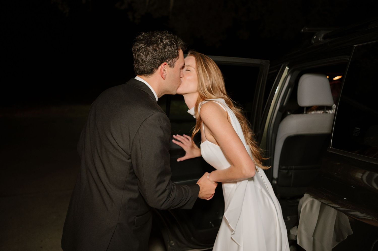 Couple departing their wedding reception at night heading towards their getaway car.