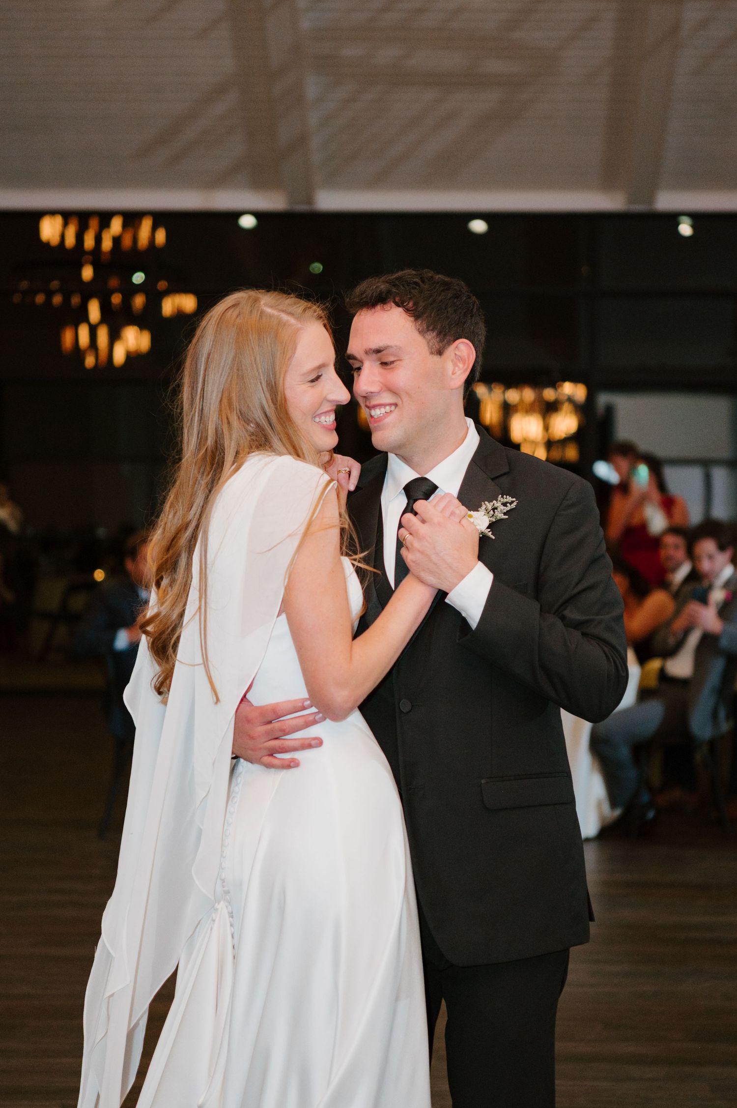 A couple shares their first dance at a wedding reception, with the bride in white and groom in black tuxedo.