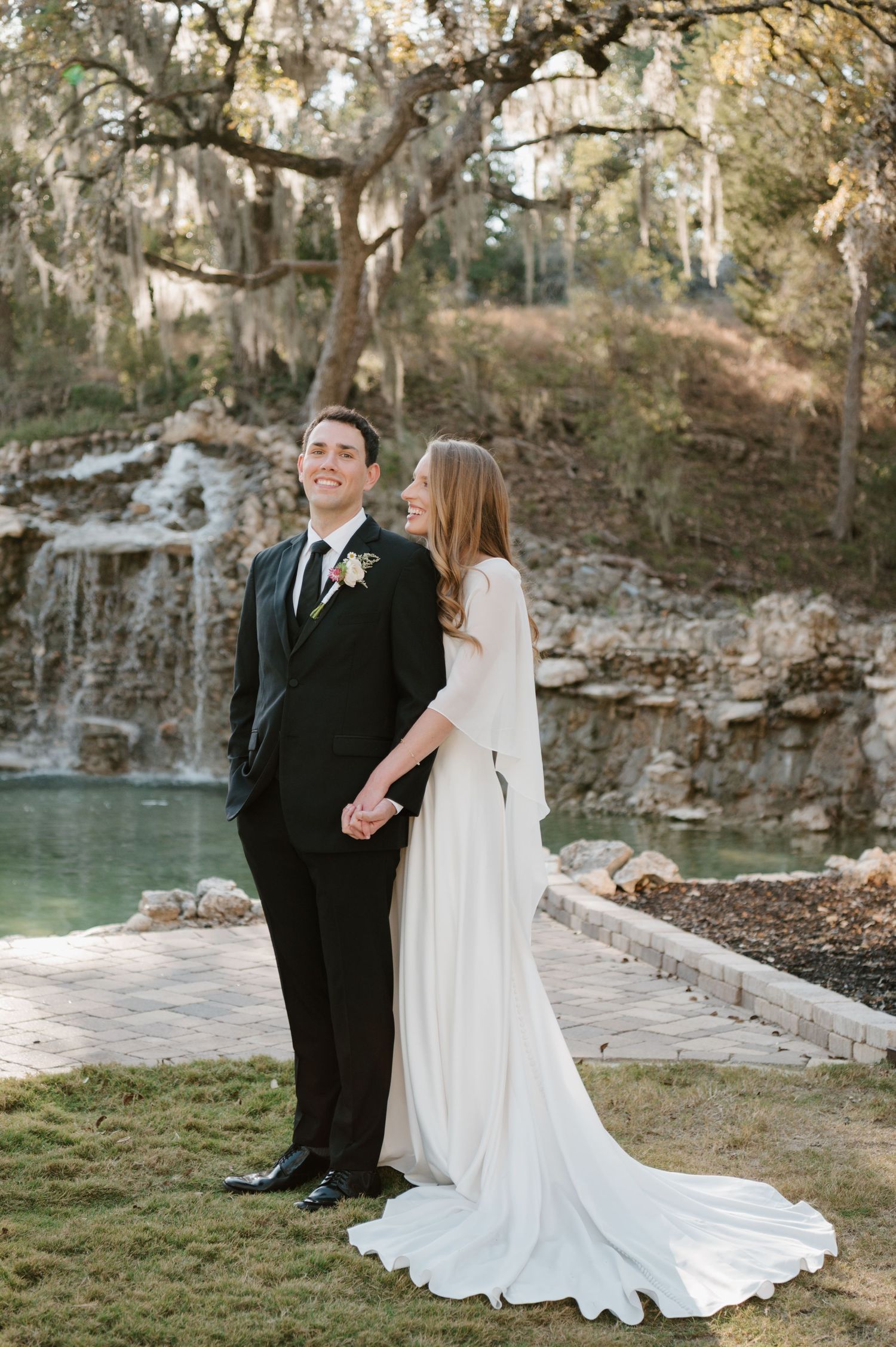 Bride and groom pose for romantic portraits near a stone waterfall and pond.