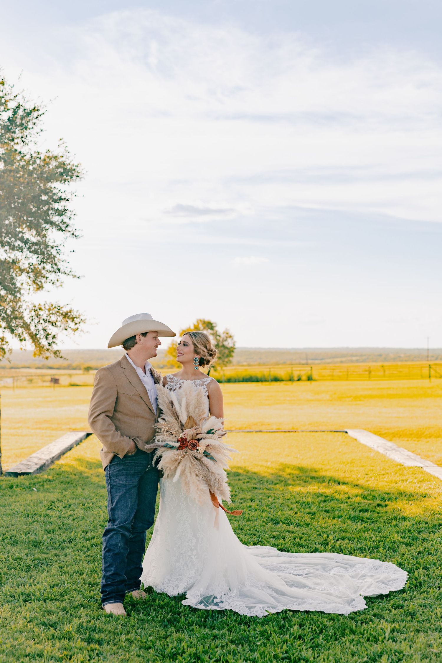 Couple in western wedding attire embracing in golden field during sunset.