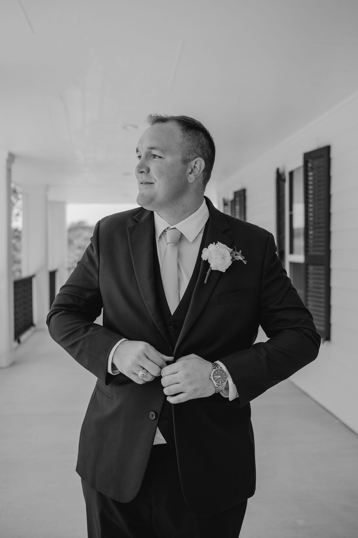 Groomsmen in black suits and ties adjusting their attire in a covered walkway.