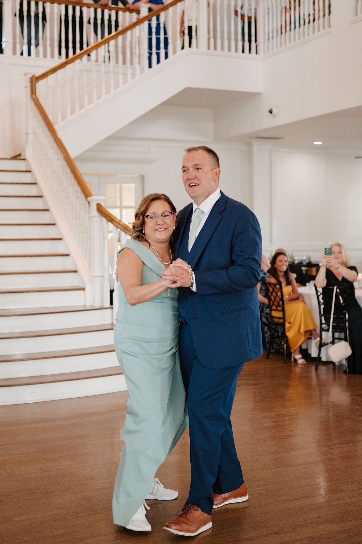 Dance celebration in an elegant white indoor venue with hardwood floors and grand staircase.