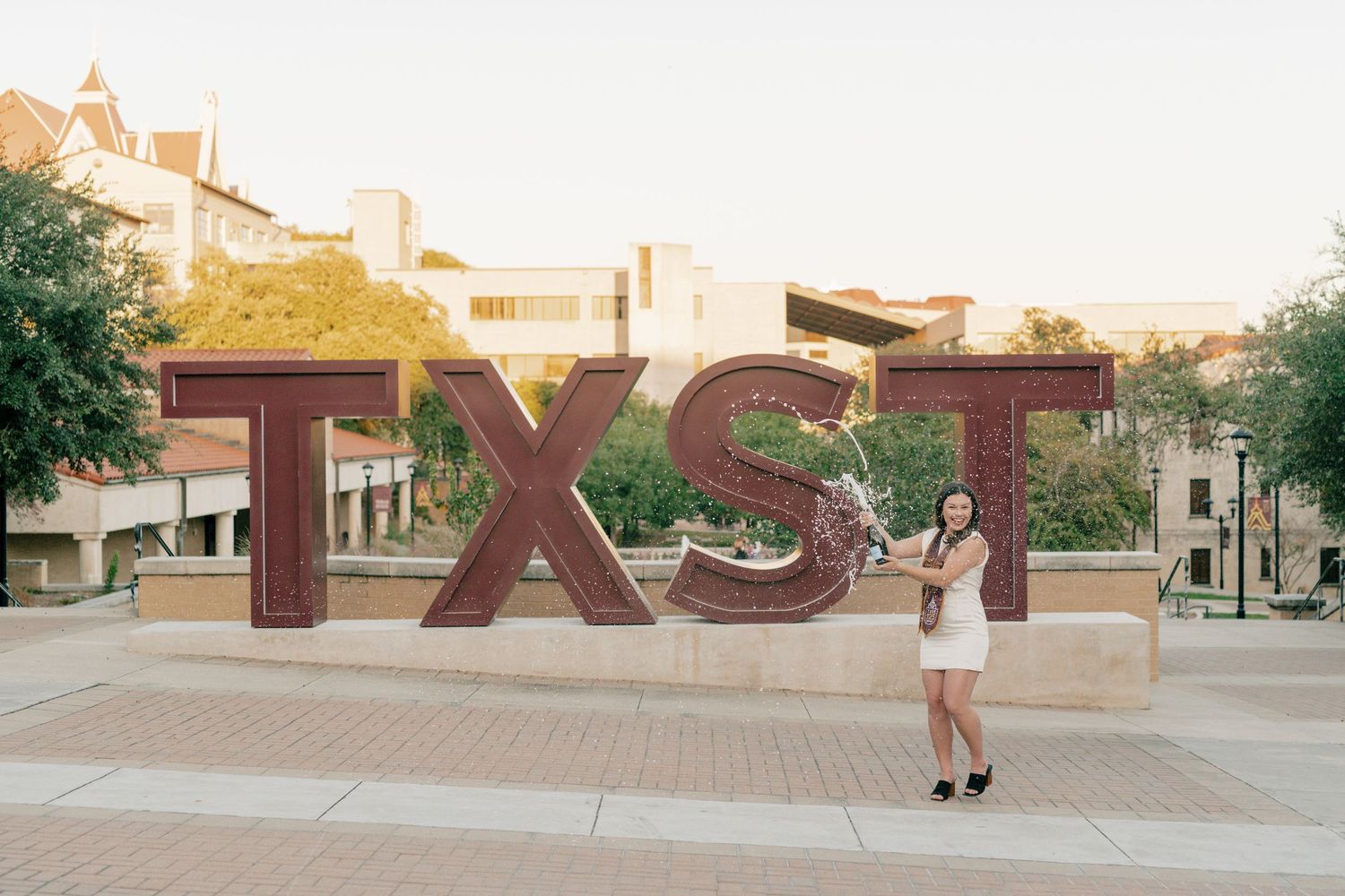 Senior session in front of large red TXST letters at sunset.