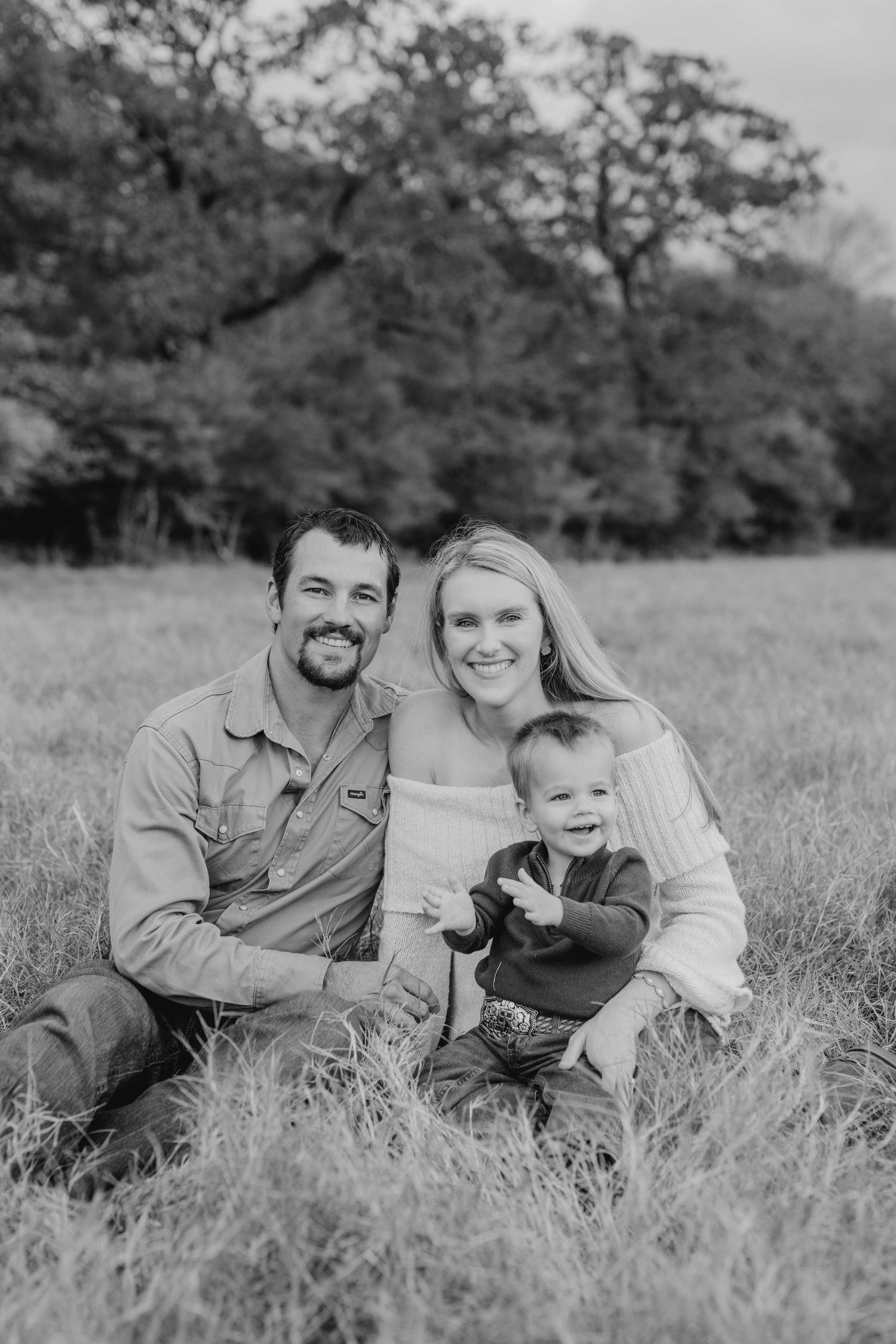 Black and white family portrait sitting together in a grassy field.