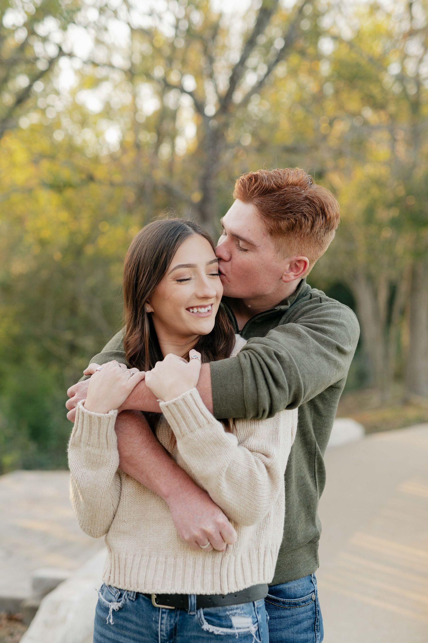 A sweet couple moment captured outdoors with golden autumn trees in the background.
