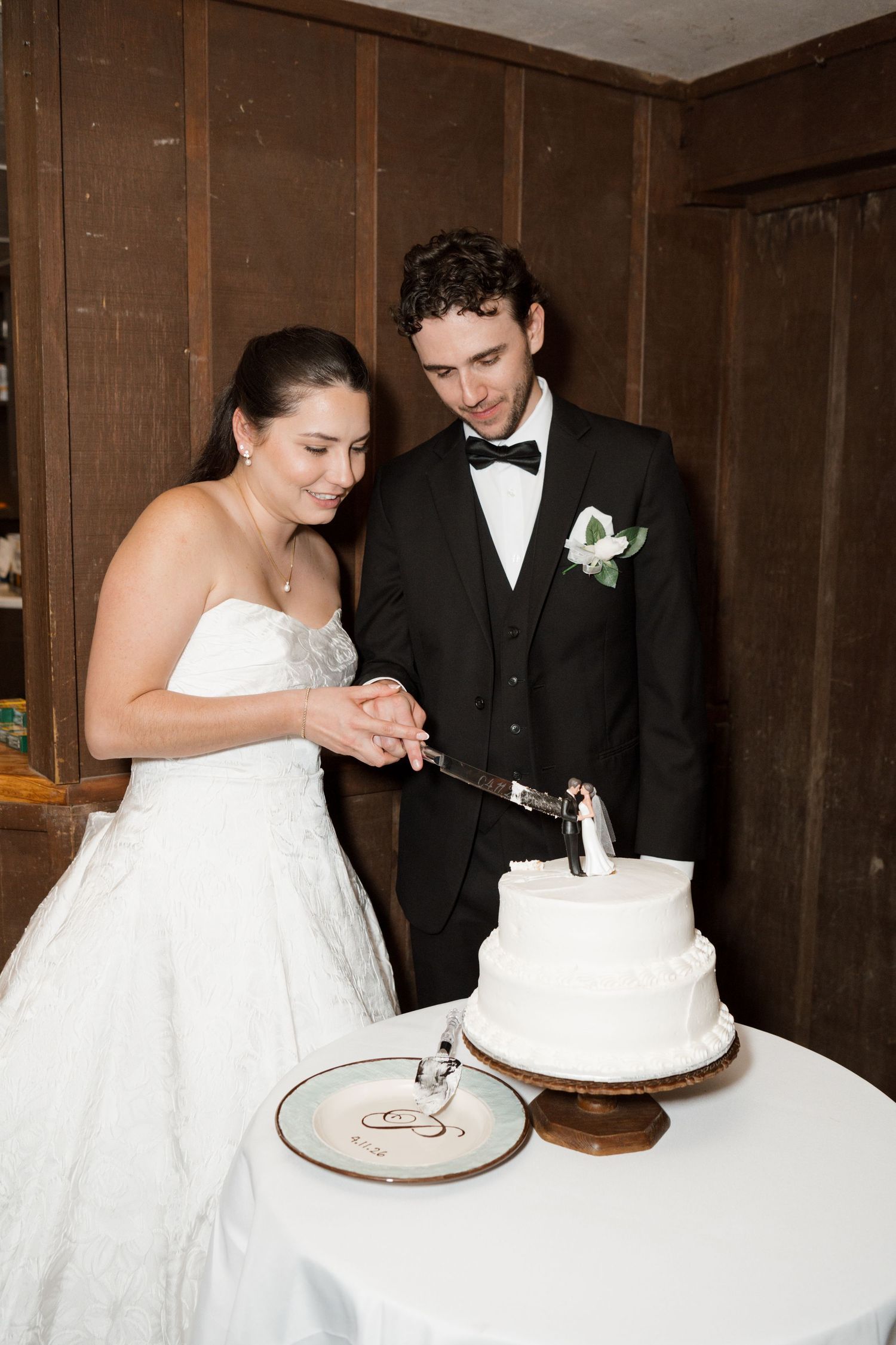 Bride and groom cutting their two-tier white wedding cake together at their wedding reception.