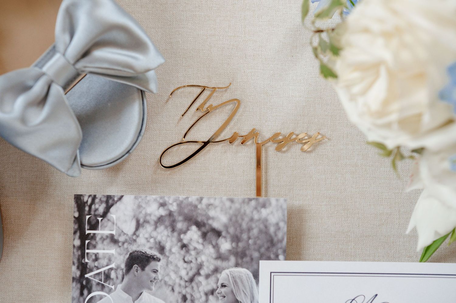 The image shows a wedding ring, a bow, and a framed photograph on a white background with floral accents.