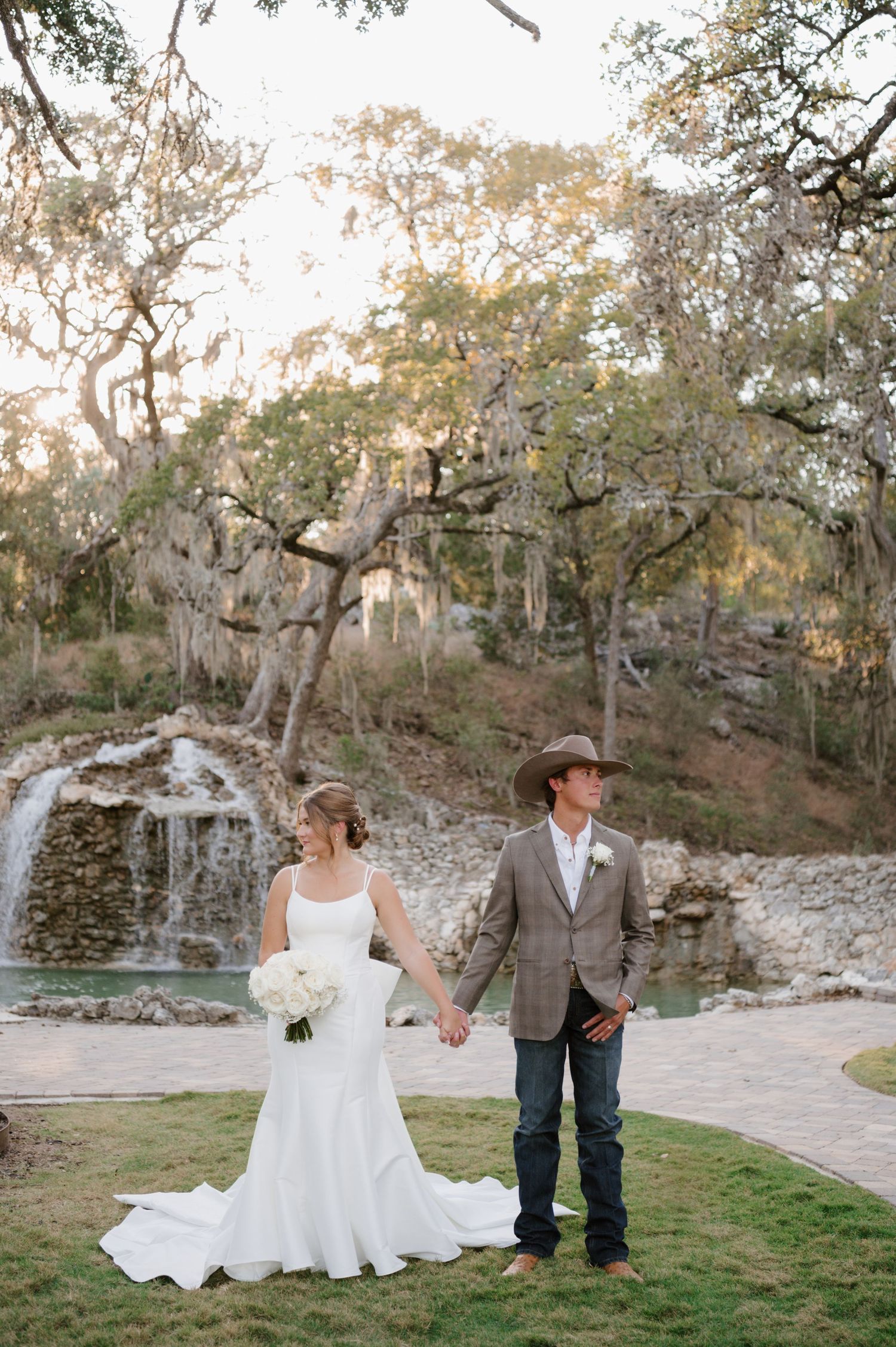 A wedding couple poses near a scenic waterfall and pond surrounded by natural rock formations.