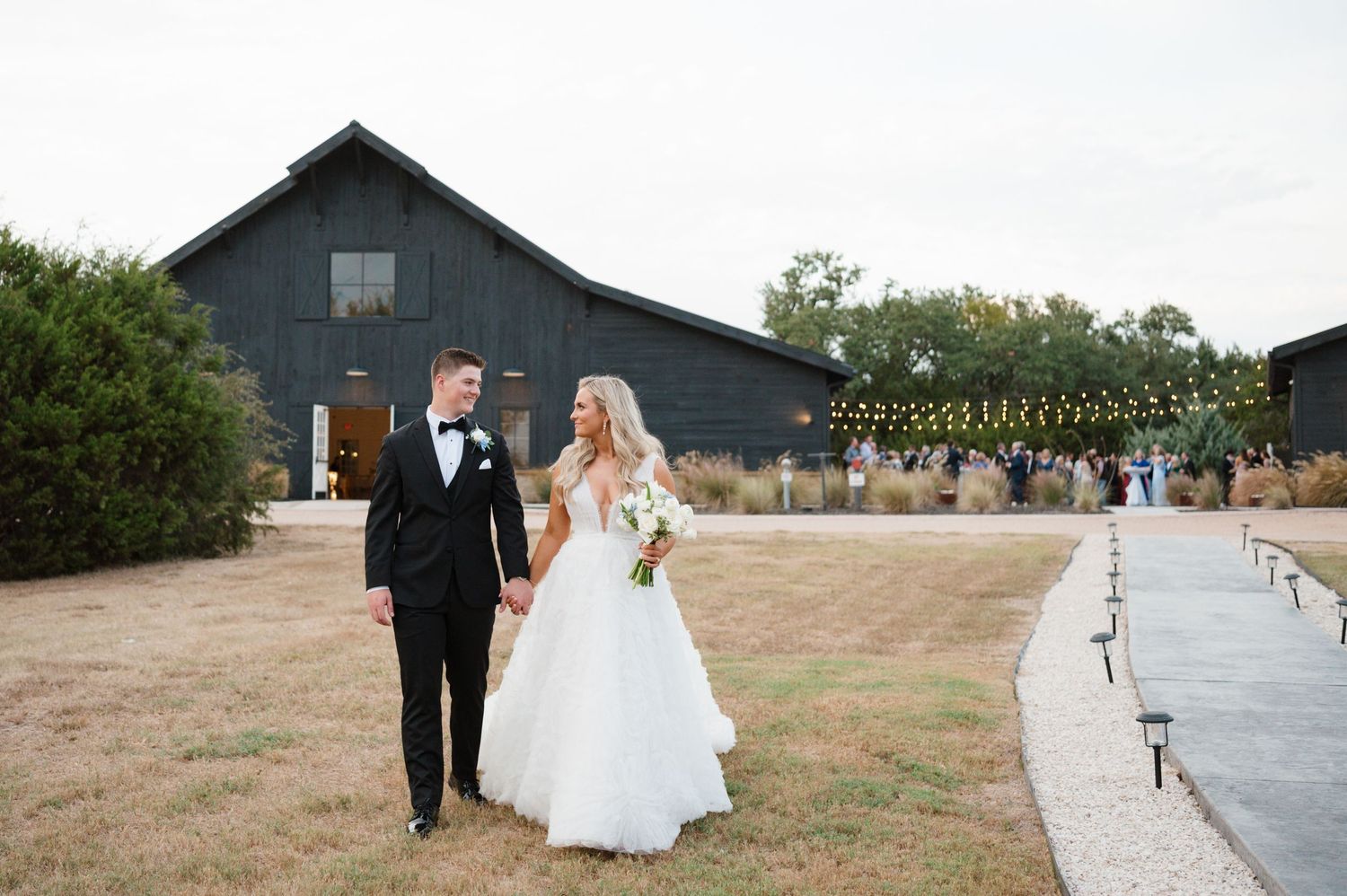 A bride and groom walk together in front of a rustic barn on their wedding day.