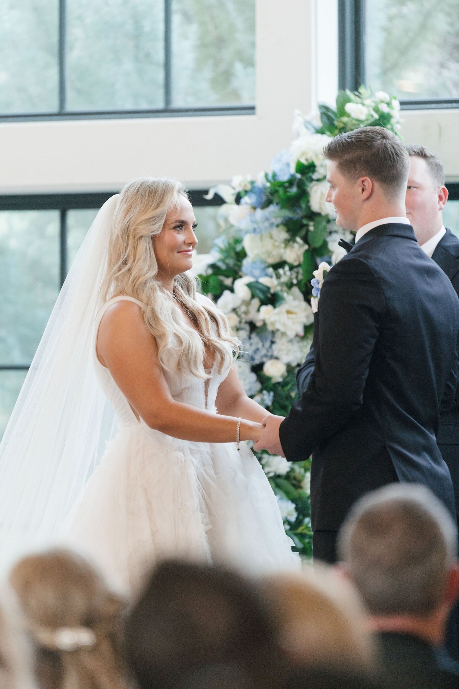 A bride and groom exchanging vows during their wedding ceremony, surrounded by guests in a beautifully decorated indoor venue.