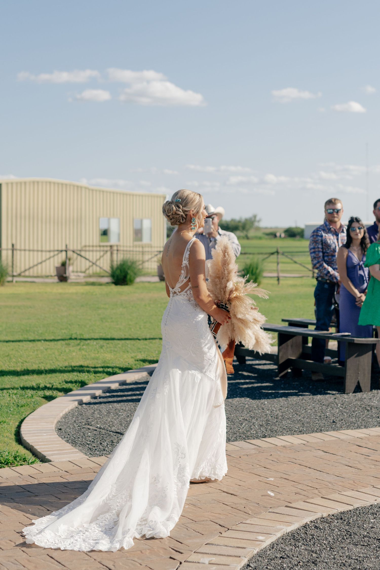 Outdoor wedding ceremony with guests seated on benches against a rural backdrop.