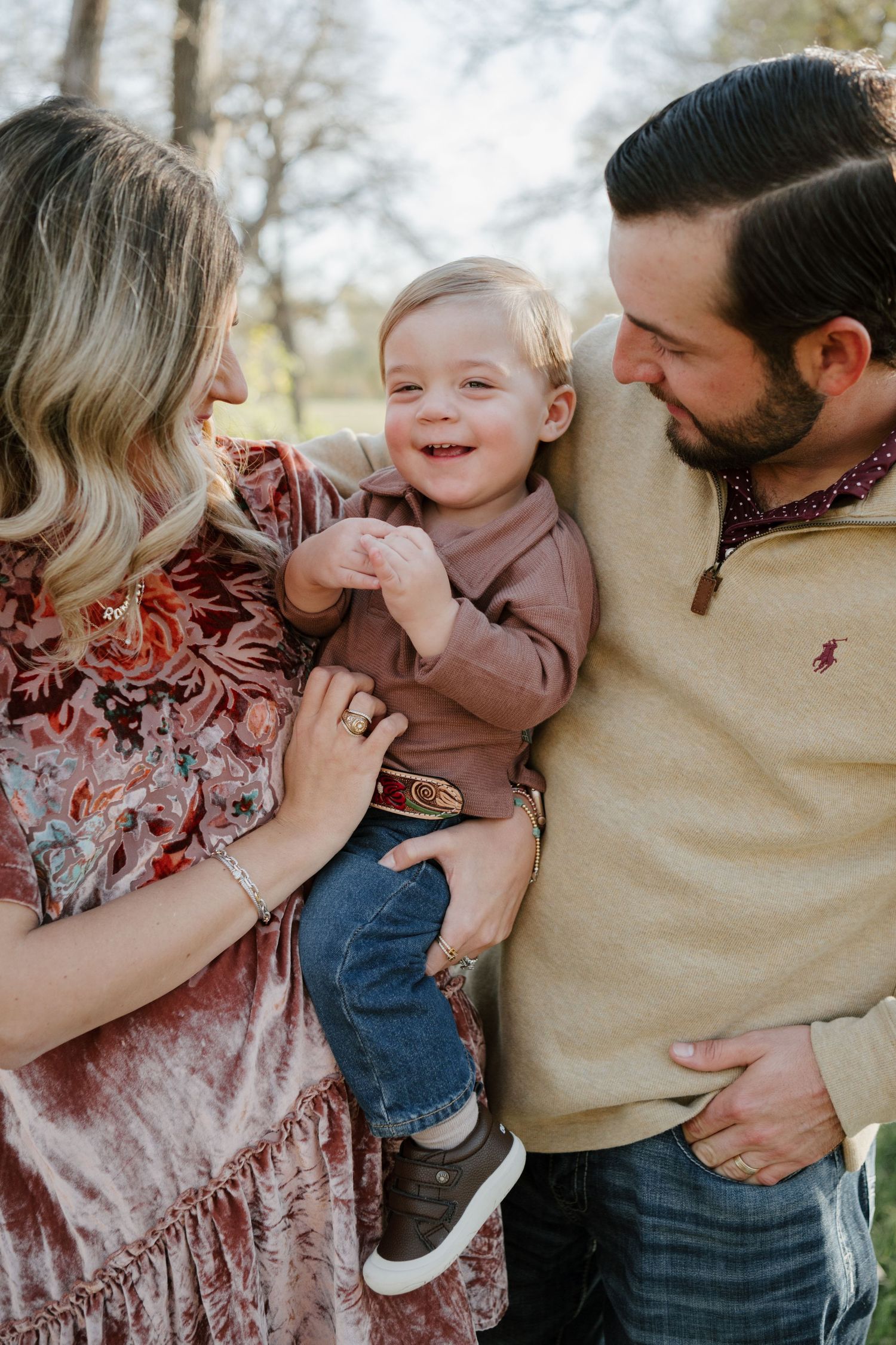 A joyful family moment captured outdoors with parents sharing a tender moment with their laughing toddler.