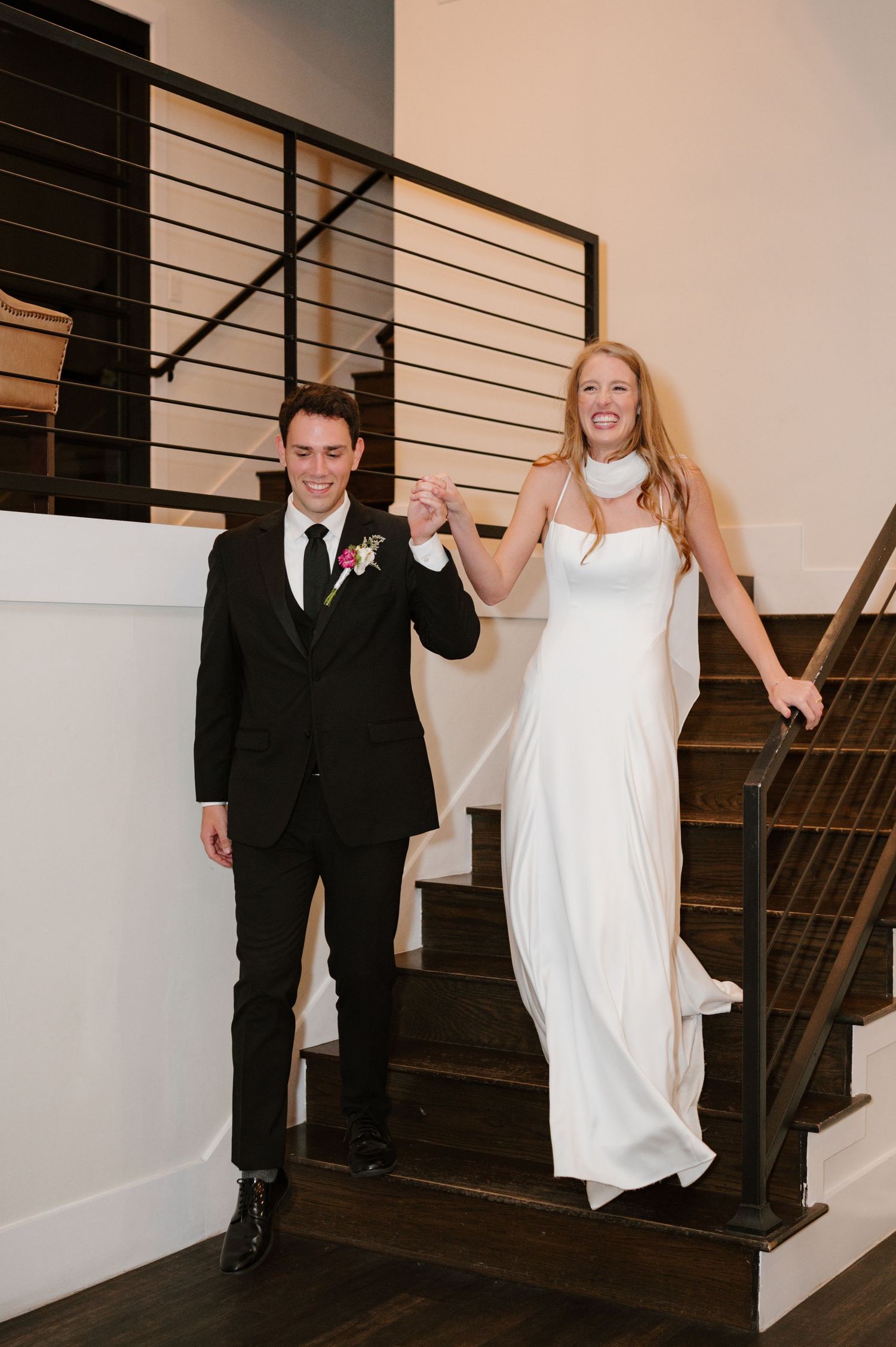 Wedding couple descending modern staircase with black railings indoors.