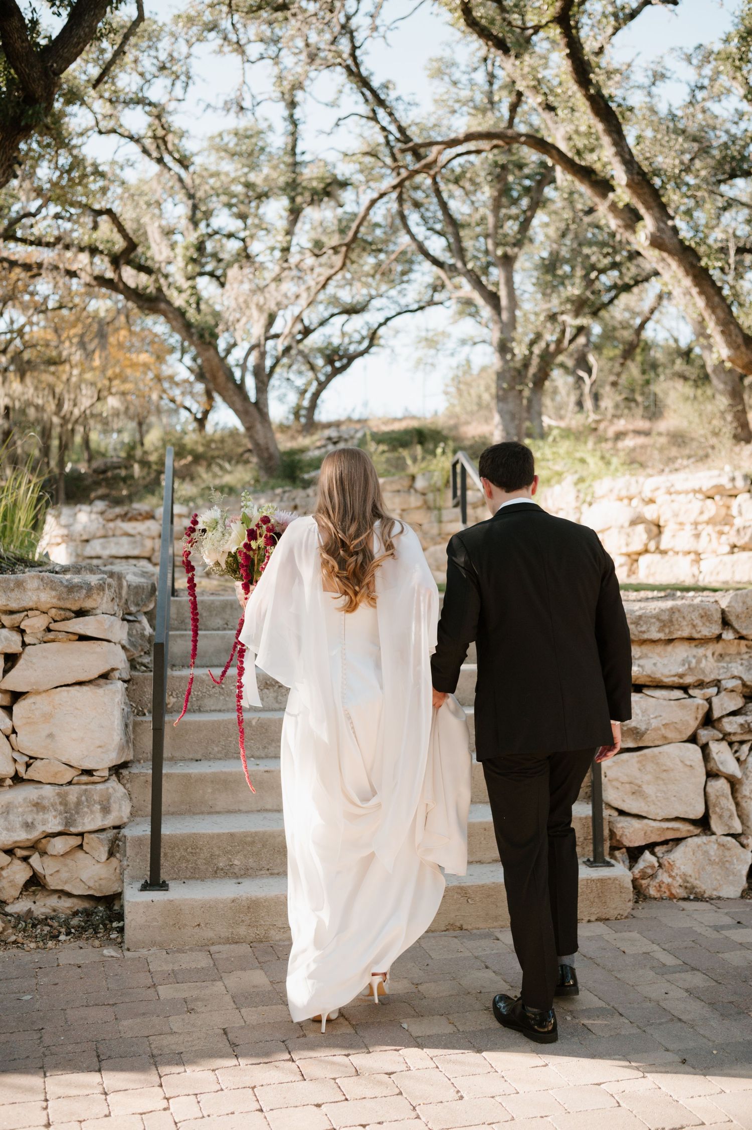 Couple walking along a stone path surrounded by oak trees on their wedding day.