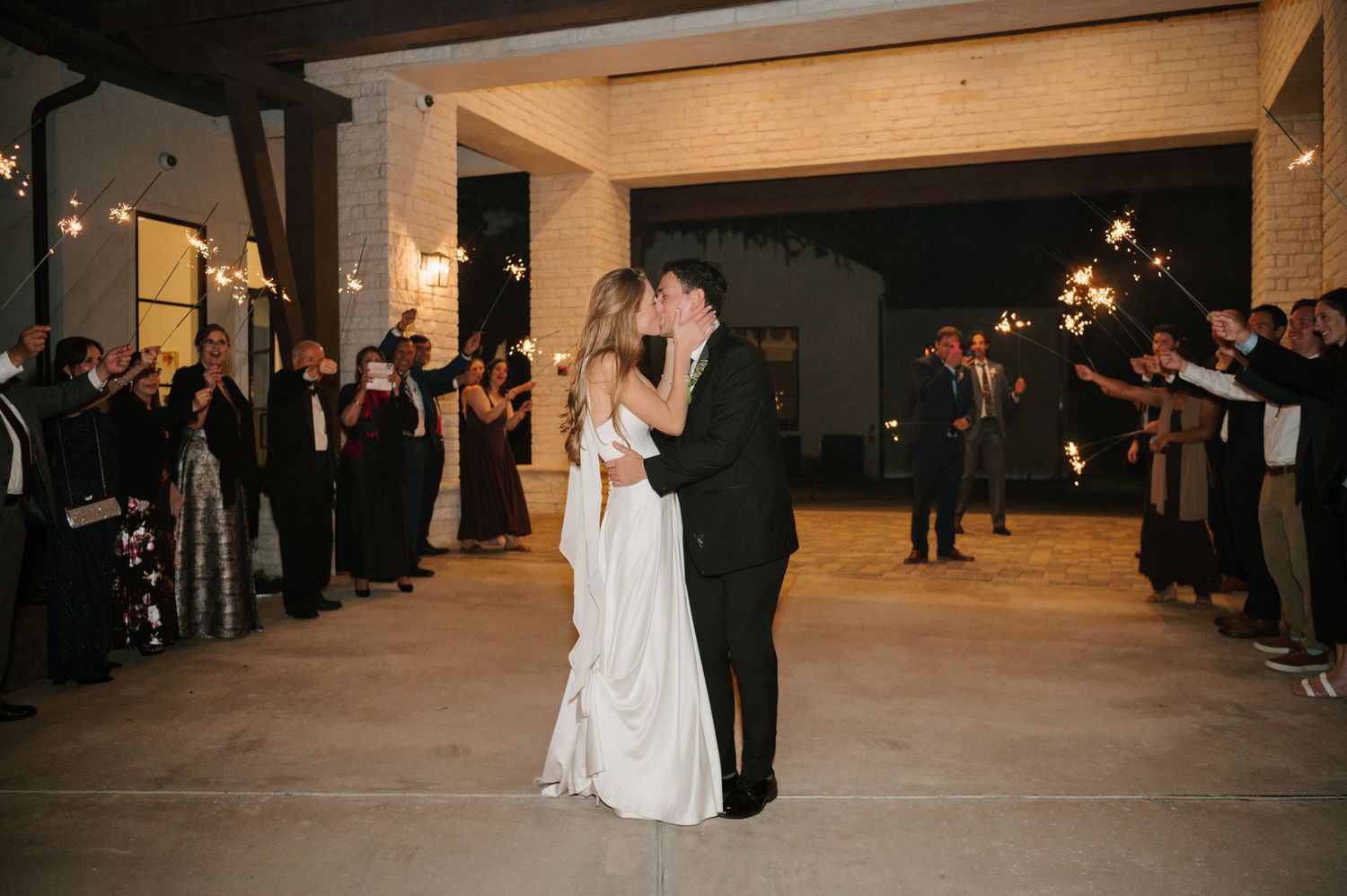 Wedding reception dance floor with guests watching couple's first dance under string lights.