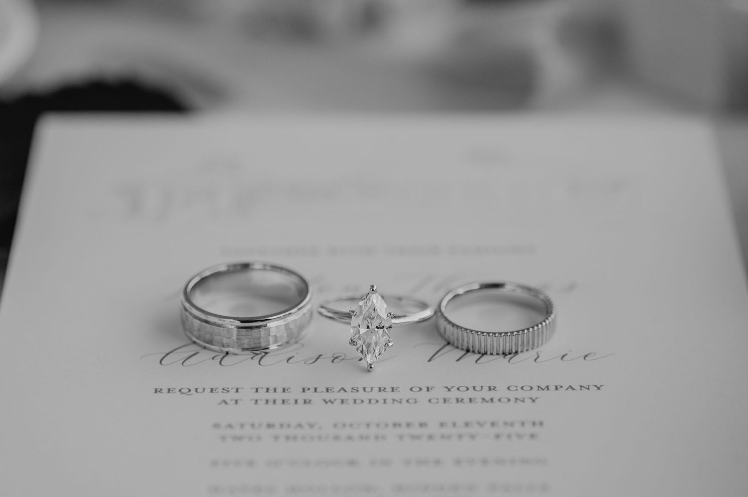 Wedding rings and invitation text photographed in black and white with soft focus.
