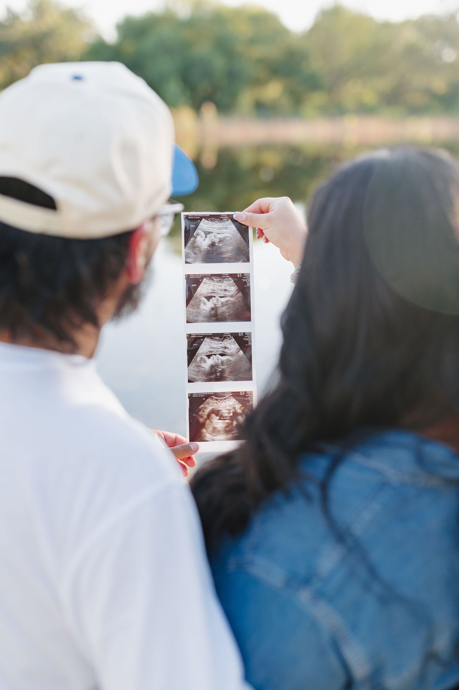Couple looks at ultrasound photos together outdoors during pregnancy announcement photoshoot.
