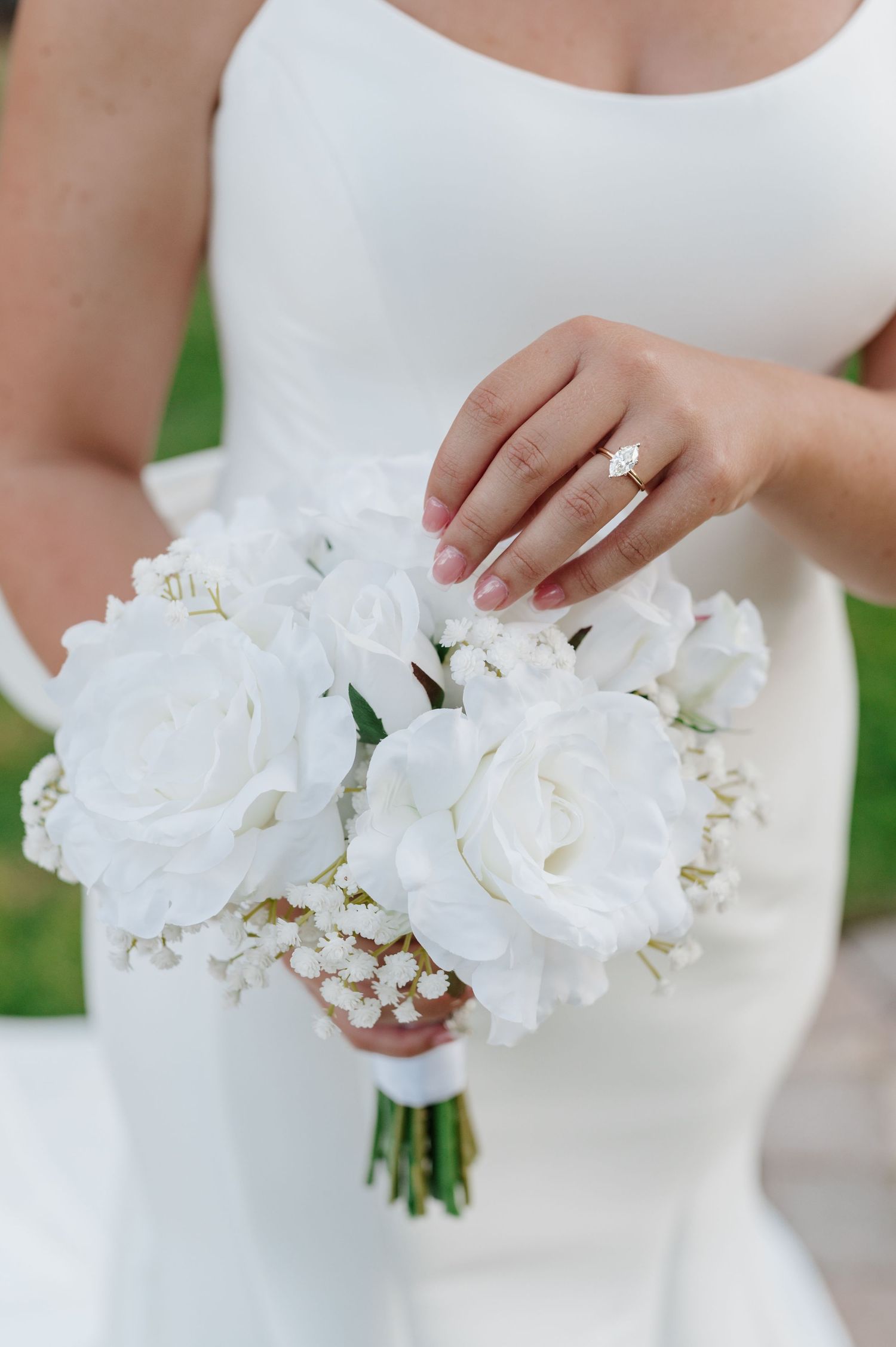 An elegant white bridal bouquet with roses and pearls showcasing a sparkling engagement ring.