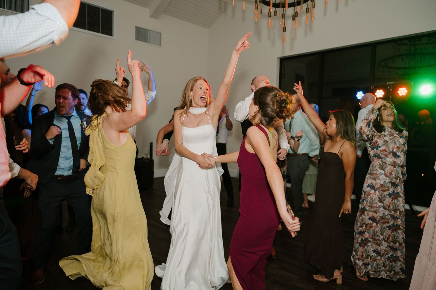 Wedding reception guests dance and celebrate on a dimly lit dance floor.