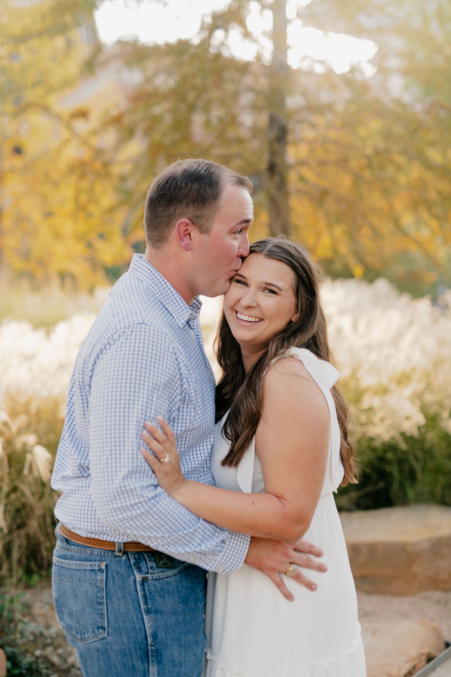 Couple sharing an intimate moment among autumn trees and ornamental grasses.