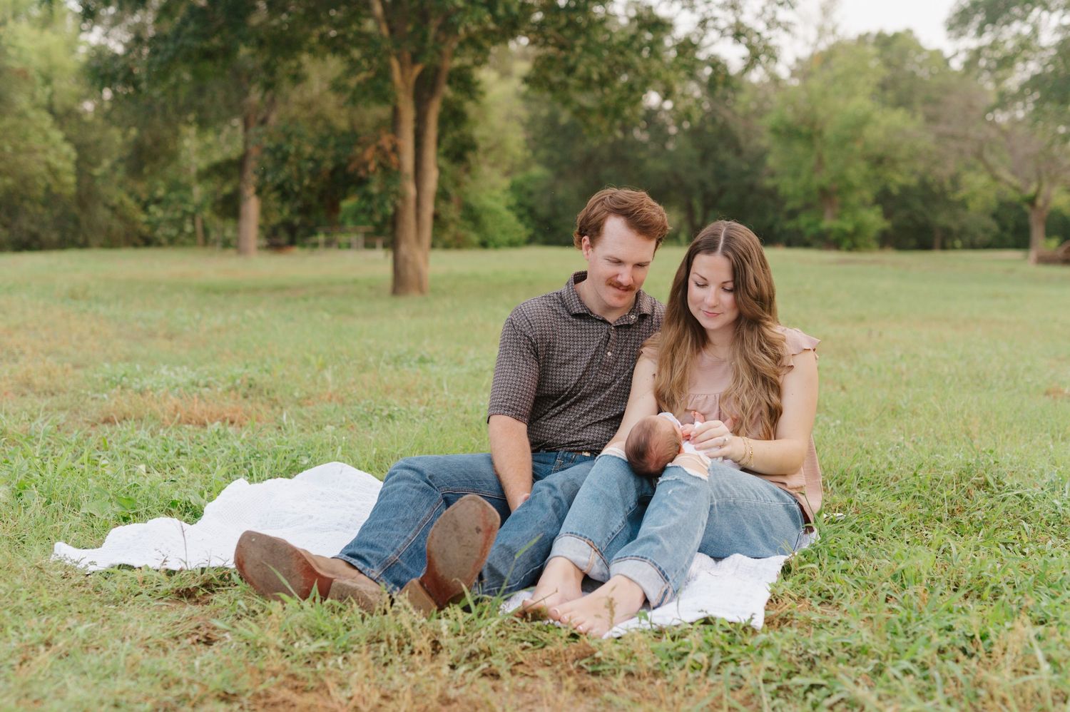 A couple lounges on a white blanket in a grassy field during an outdoor photo session.